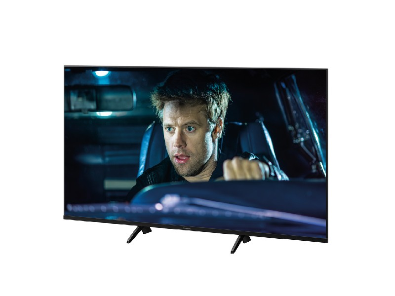 Una pantalla de TV que muestra a un hombre en un coche, con aspecto sorprendido. Fondo oscuro.