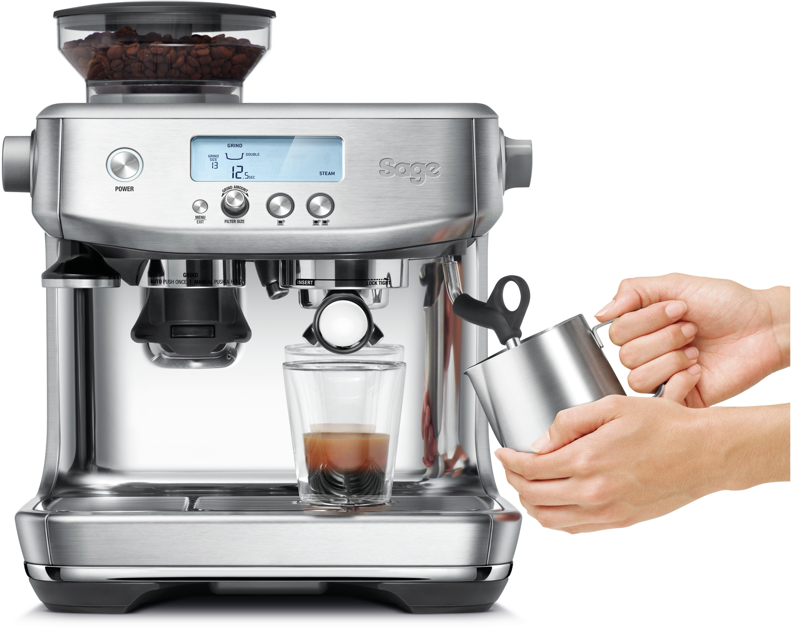 A stainless steel espresso machine, with a person pouring milk.  A glass and coffee beans are visible.
