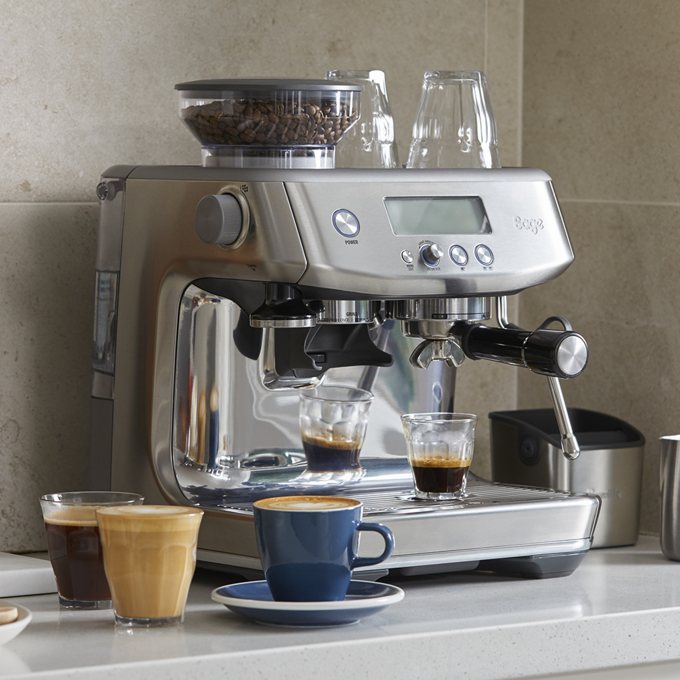 An espresso machine with coffee cups and a person preparing coffee, with coffee beans in a container.