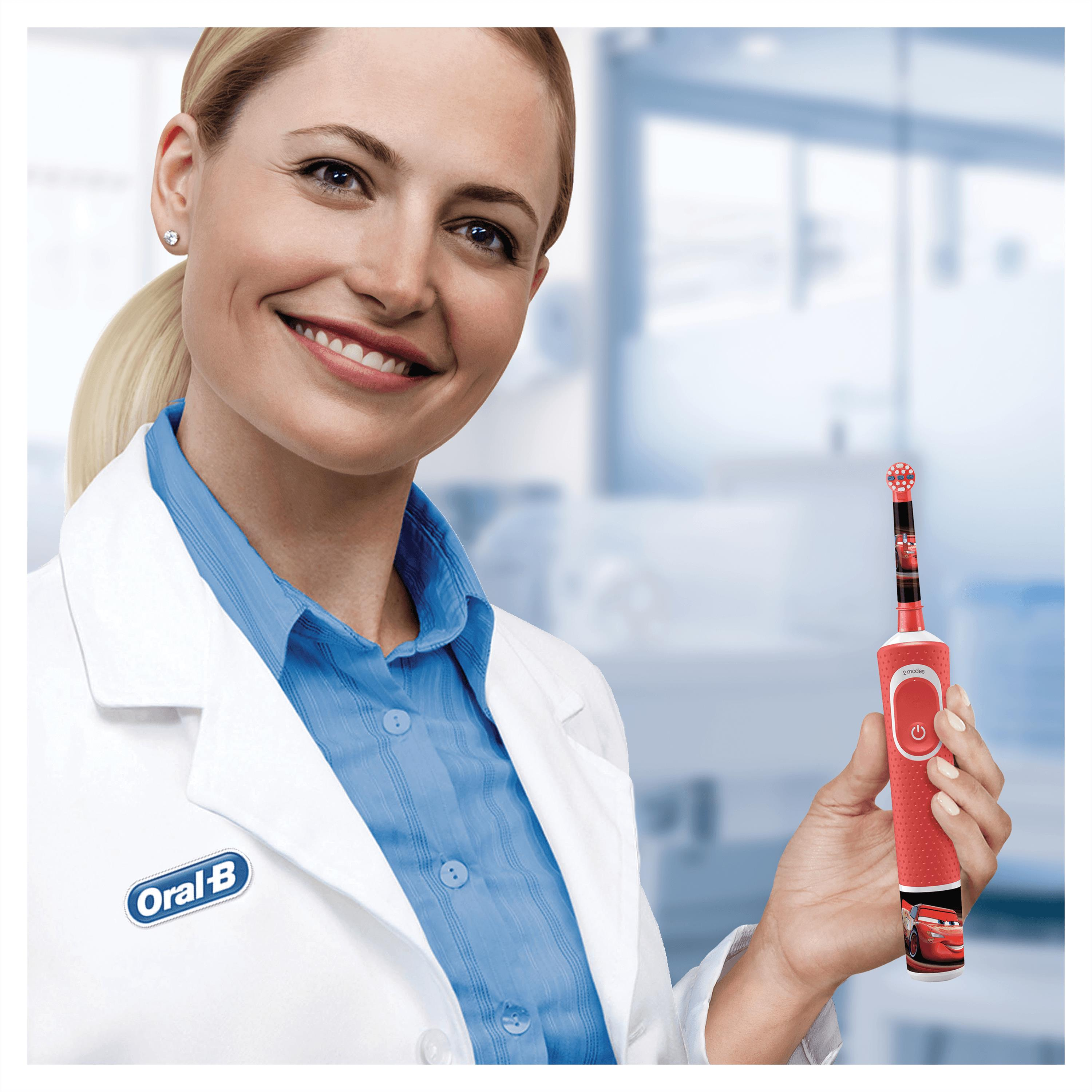 Eine Frau im Laborkittel hält eine rote elektrische Zahnbürste von Oral-B mit 'Cars'-Design.