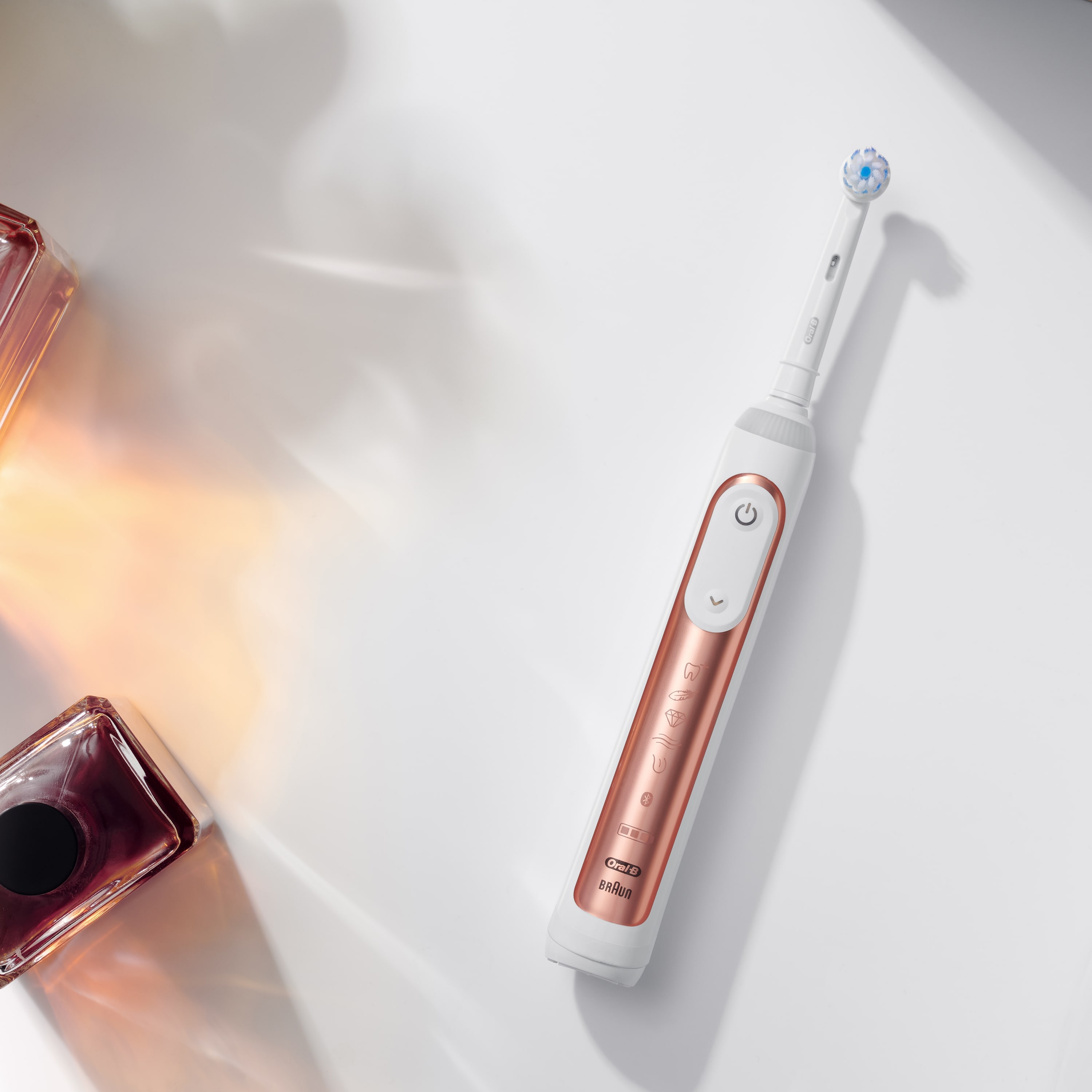 Elektrische Zahnbürste in Weiß und Roségold mit zwei Parfümflaschen, Draufsicht.