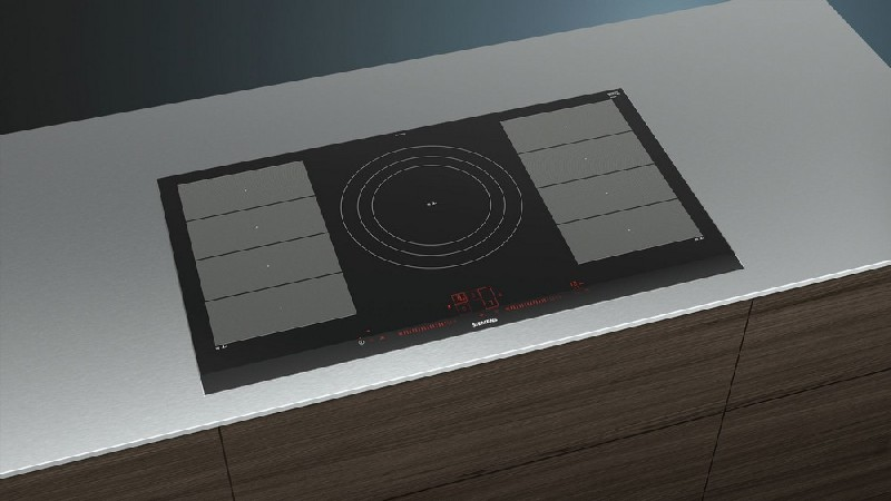 Placa de inducción negra sobre una encimera plateada.