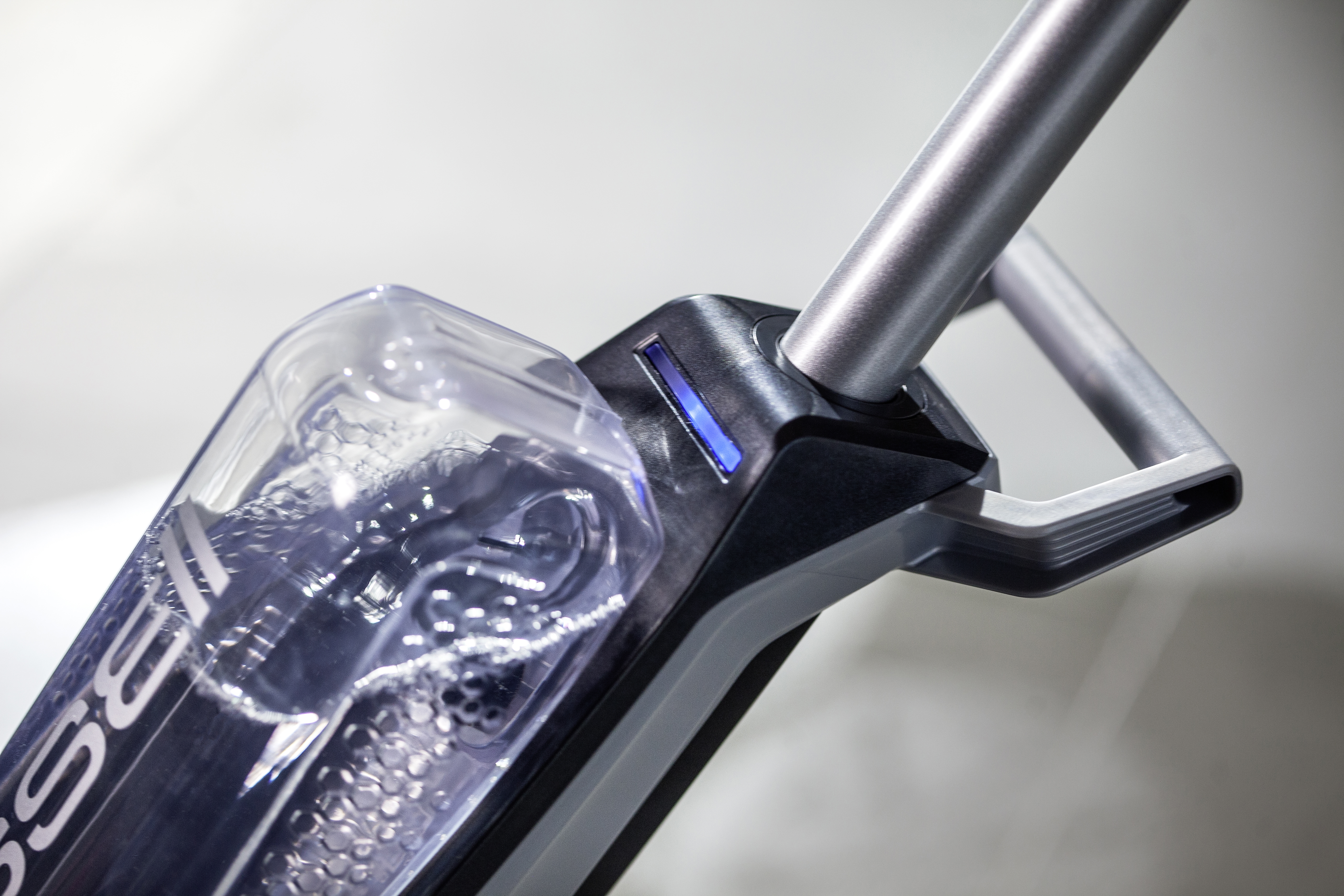 Nahaufnahme eines Reinigungsgeräts. Transparenter Wasserbehälter, grauer Griff.