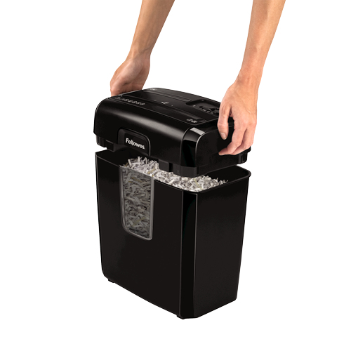 Manos levantando la cabeza de una destructora Fellowes negra de un contenedor lleno de papel triturado.
