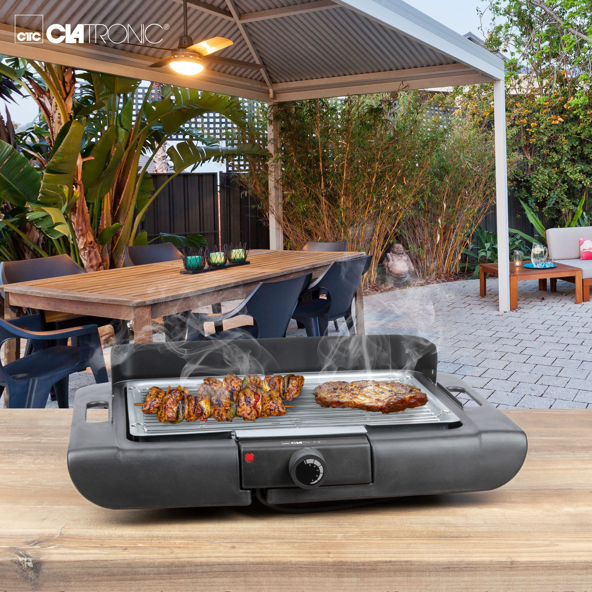 Schwarzer Elektrogrill auf einem Holztisch mit gegartem Essen. Terrasse mit Holztisch im Hintergrund.