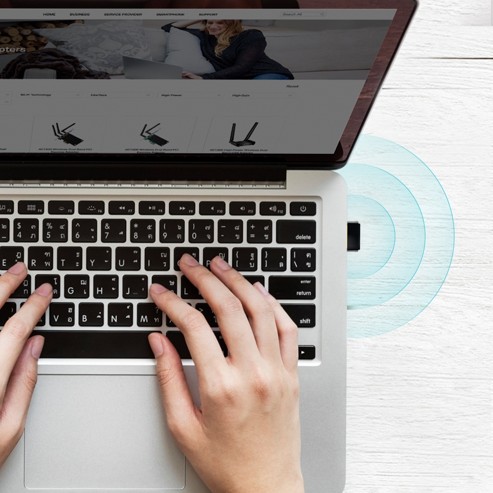 Un laptop mostra un sito web. Le mani digitano sulla tastiera, con un adattatore wireless collegato.