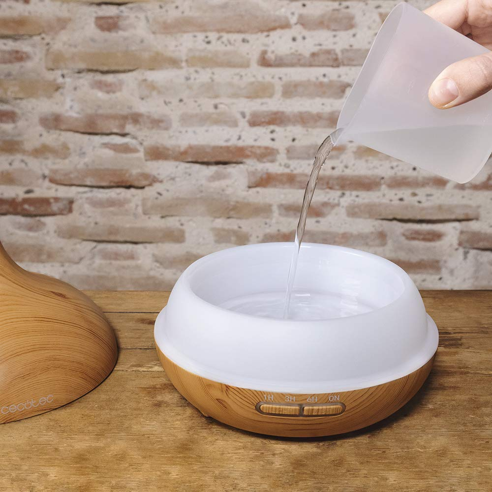 Una persona vierte agua en un difusor blanco y color madera. Los botones están iluminados.