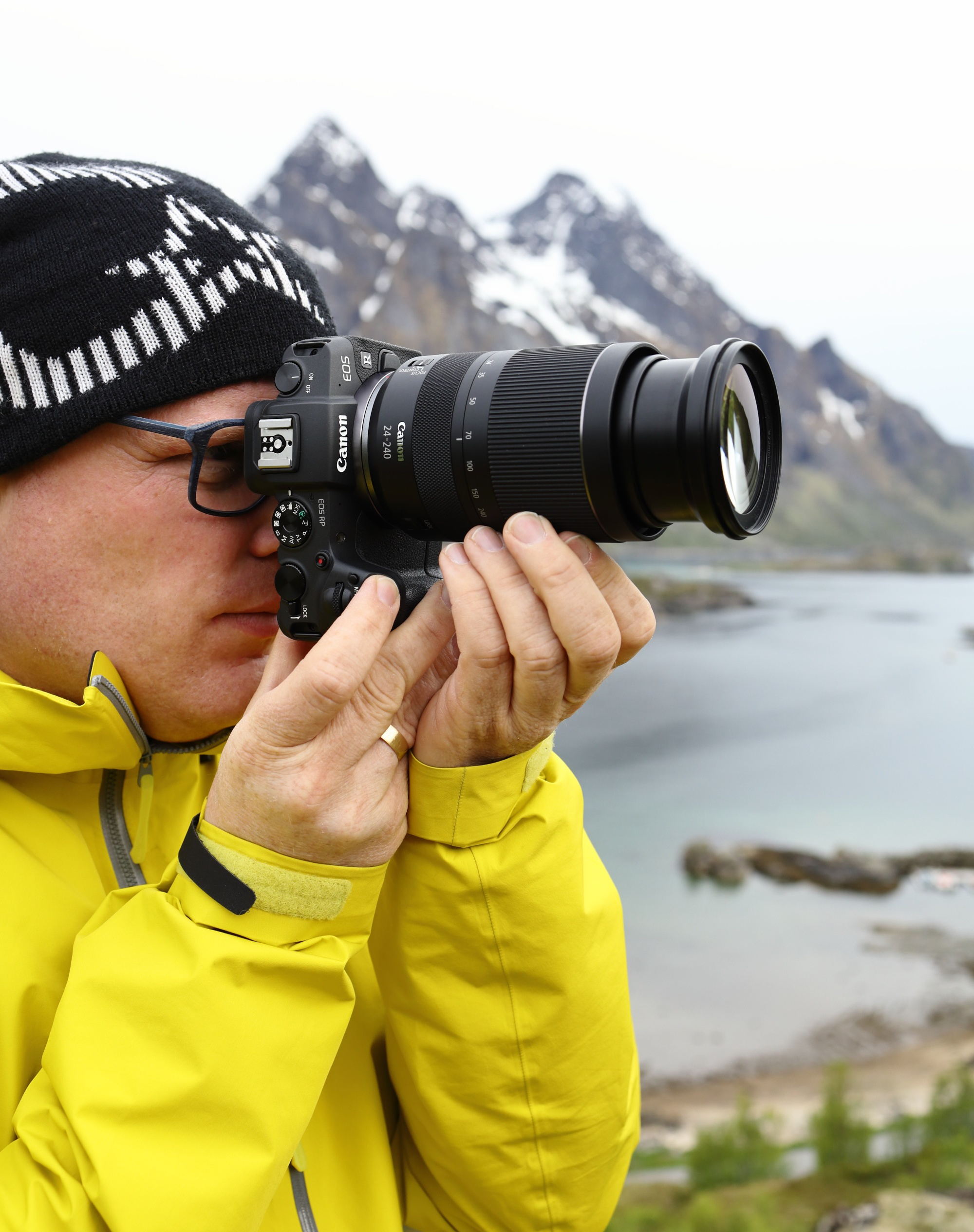 Ein Mann in gelber Jacke und Hut macht ein Foto mit einer Kamera.