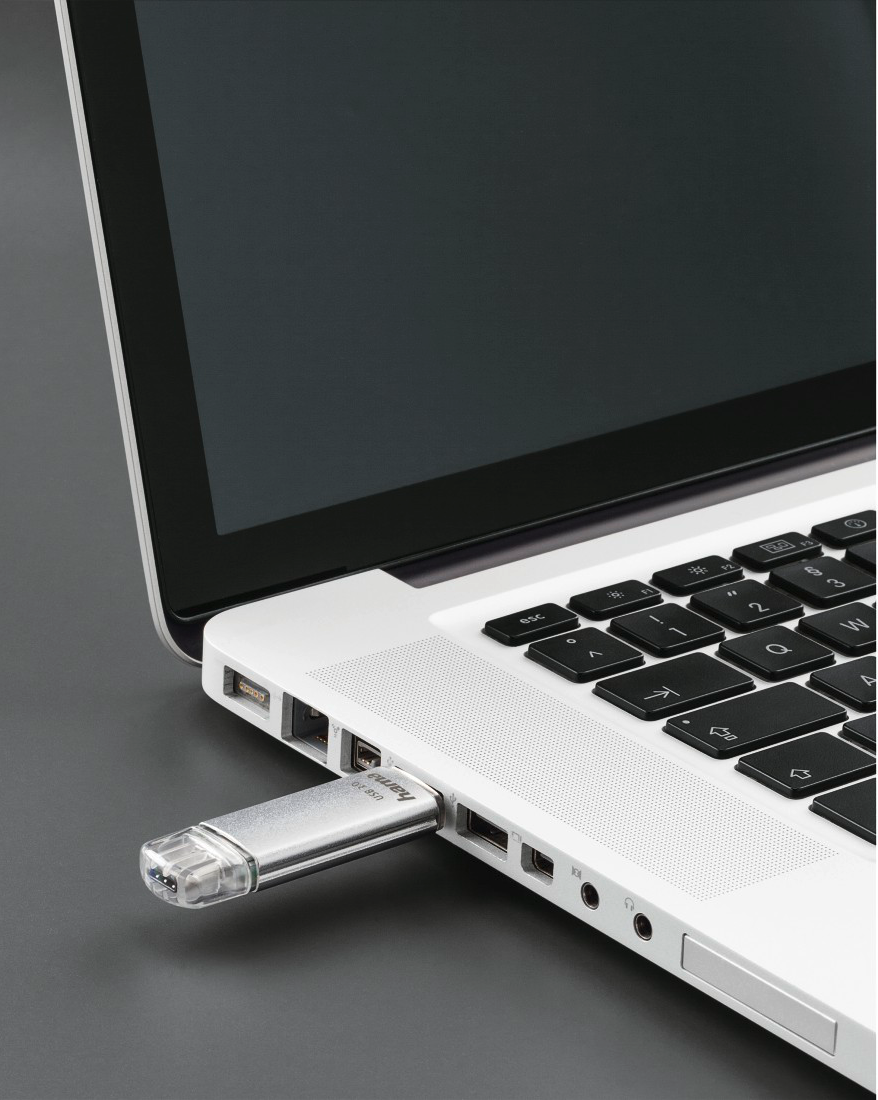 Une clé USB argentée est branchée sur un ordinateur portable. L'ordinateur portable est argenté et le fond est gris.