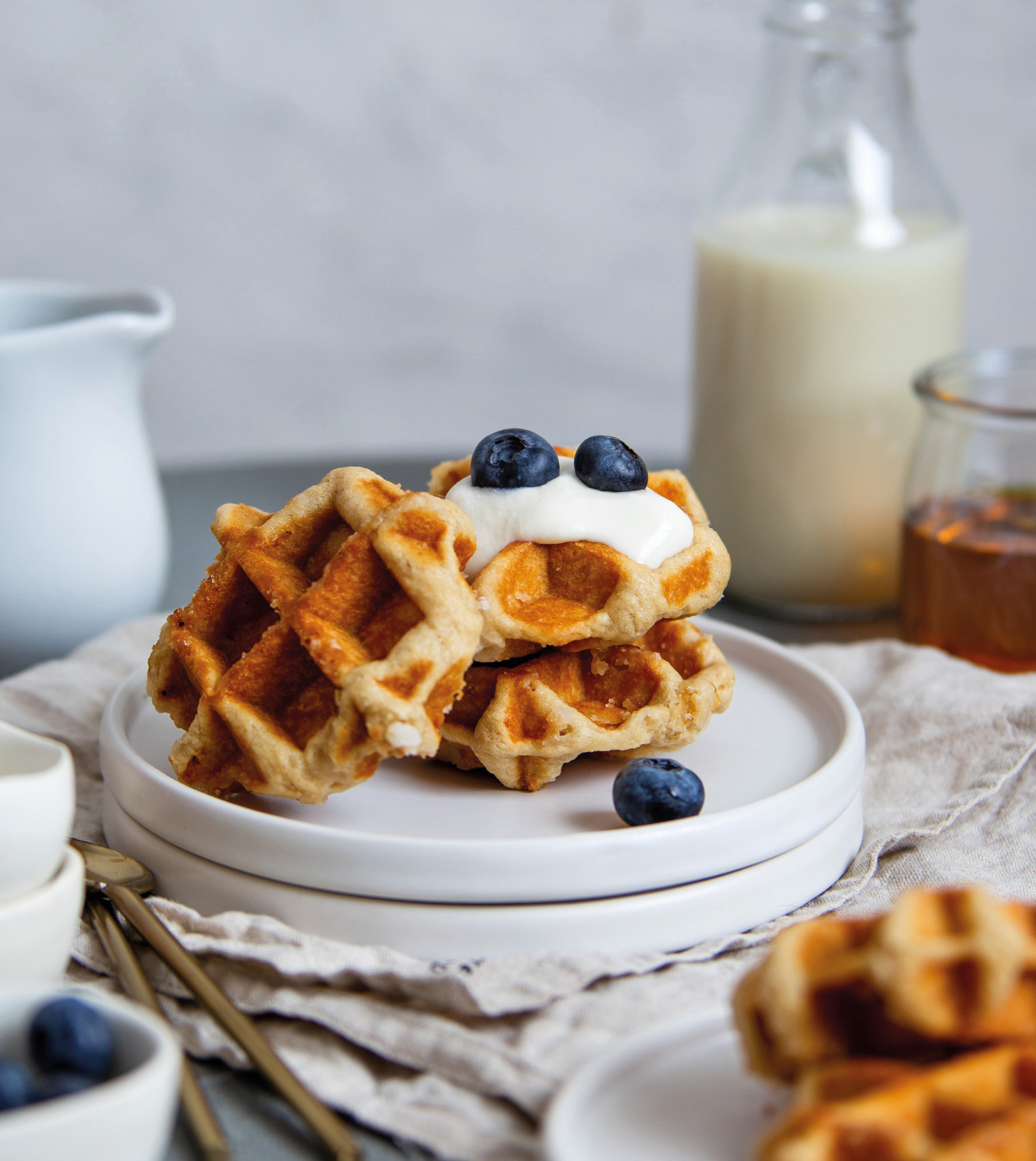 Waffeln mit Blaubeeren und Sahne, serviert auf weißen Tellern mit einer Milchflasche.