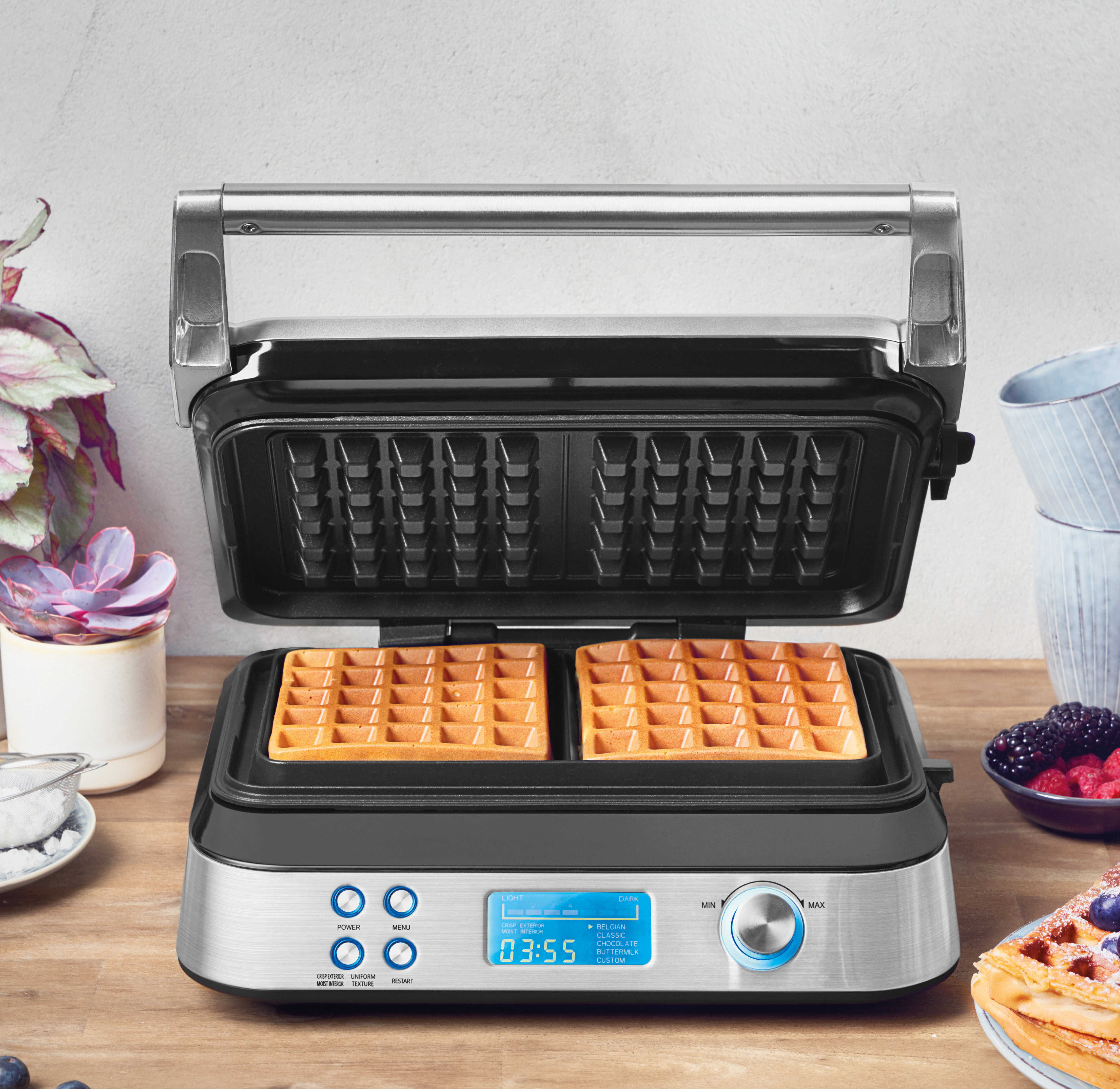 Waffeleisen mit zwei Waffeln. Digitalanzeige zeigt Zeit, mit Blume und Beeren.