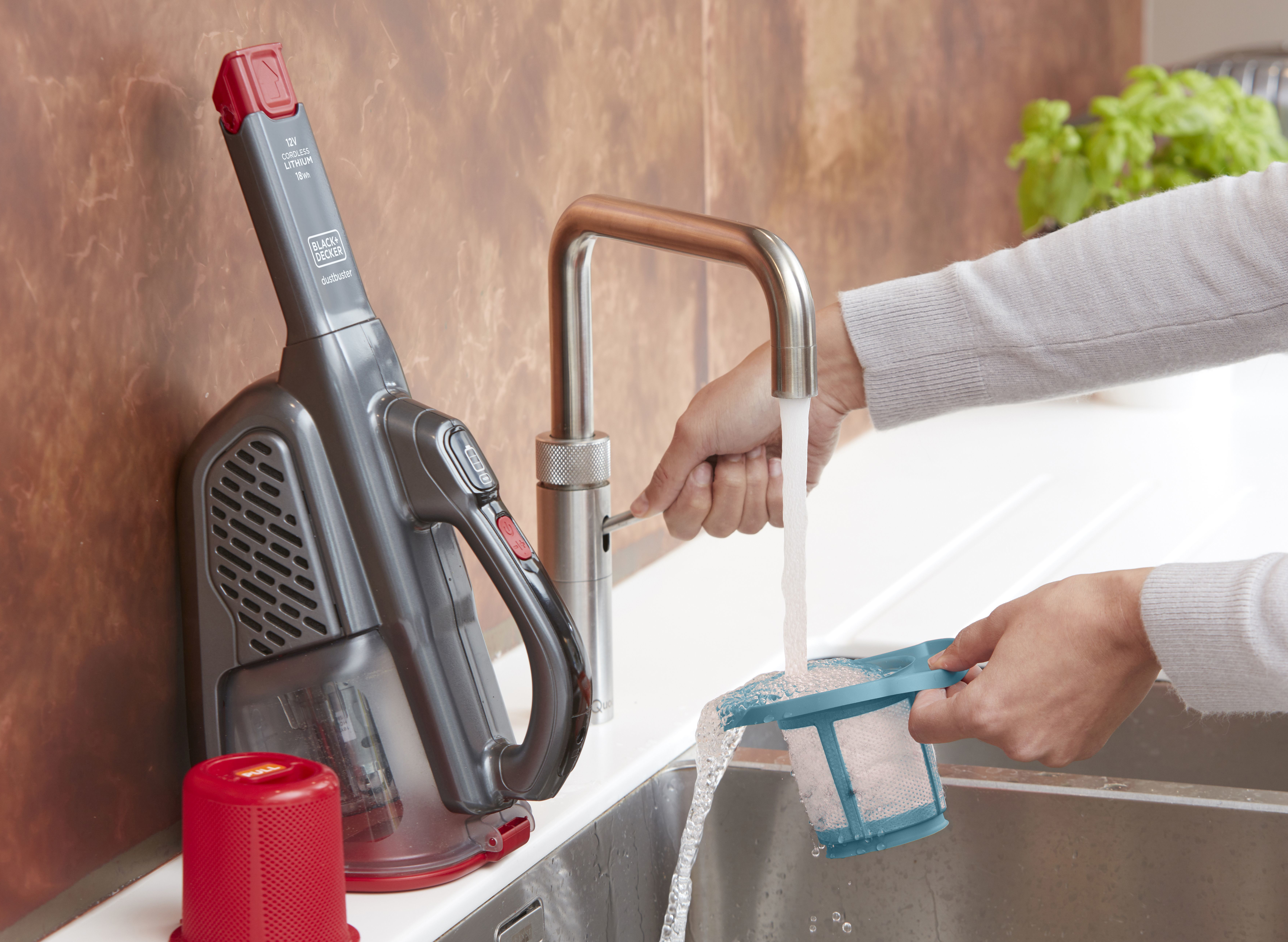 Eine Person reinigt einen Staubsaugerfilter unter einem laufenden Wasserhahn in einem Waschbecken.