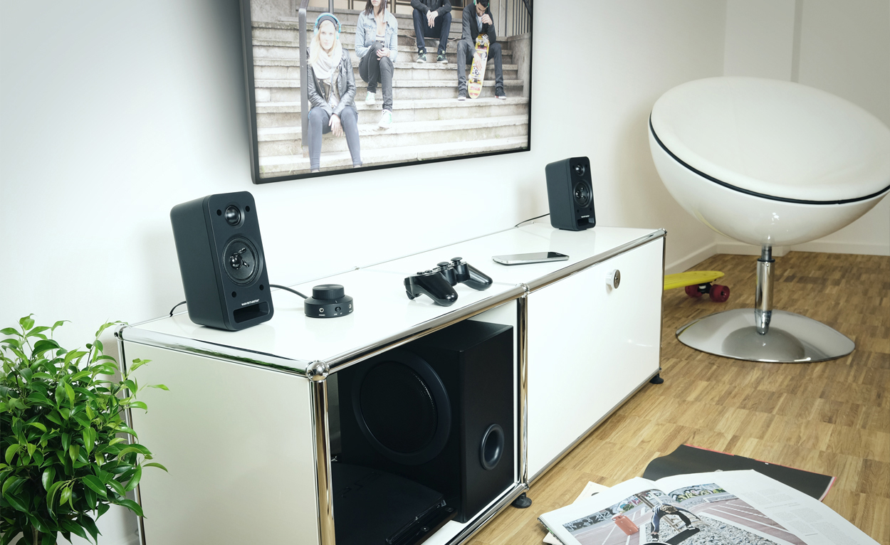 Wohnzimmer-Setup mit Lautsprechern, Fernseher und Unterhaltungsgeräten auf einem weißen Schrank, mit Pflanze.