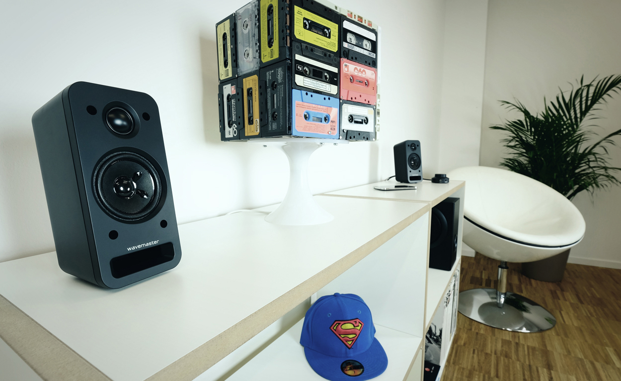 Modernes Wohnzimmer mit Lautsprecher, Kassettenband-Kunstwerk und weißem Stuhl.
