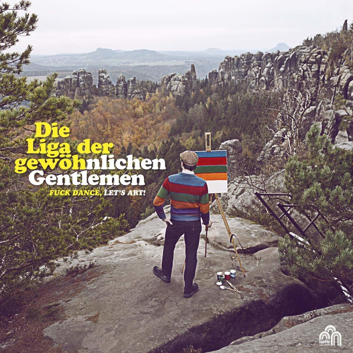 Ein Mann malt auf einer Leinwand, die auf einem Felsen aufgebaut ist, mit einer Berglandschaft im Hintergrund.