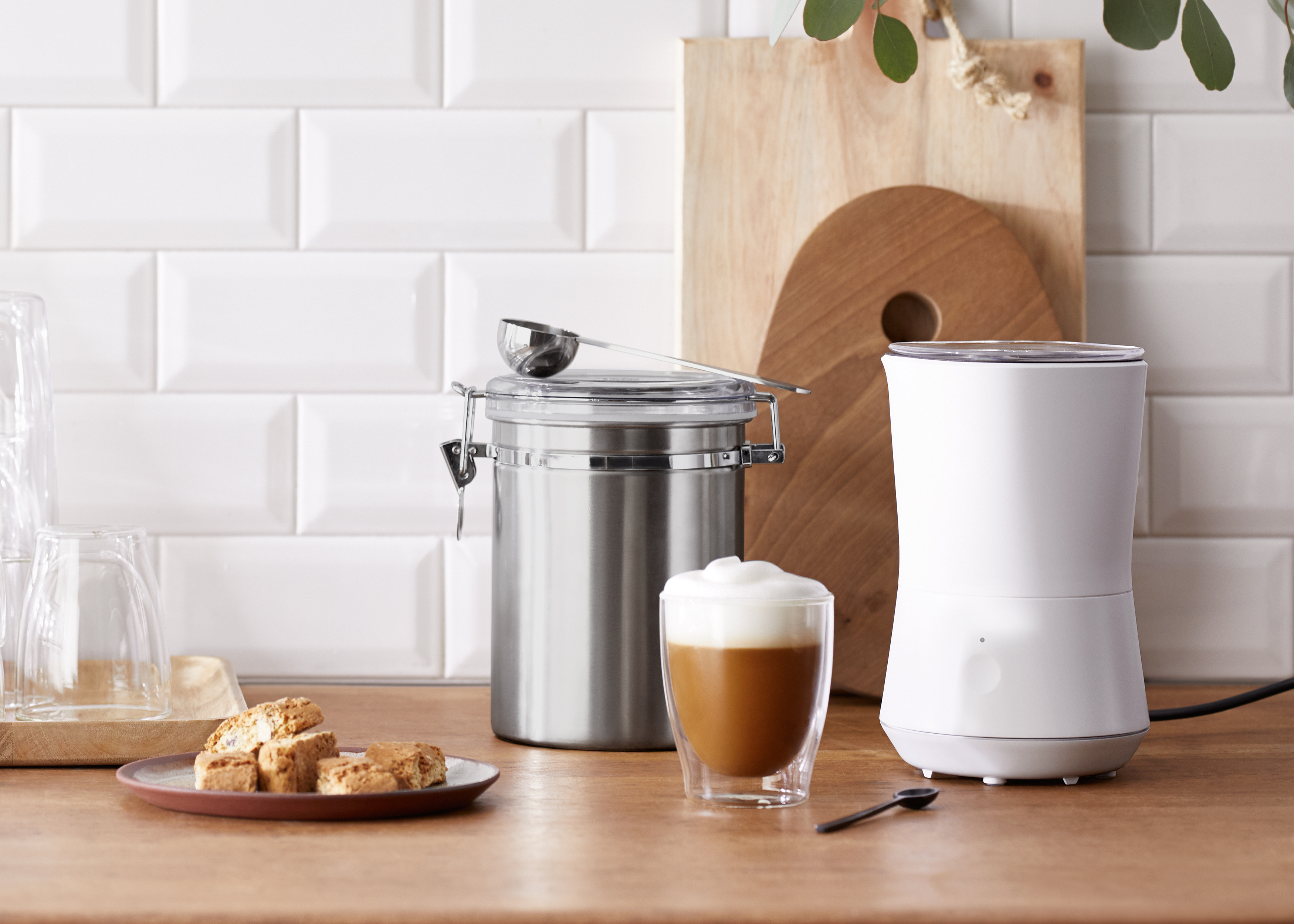 Küchenszene: Kaffeemühle, Kaffeebehälter und ein Glas Latte auf einer Holztheke.