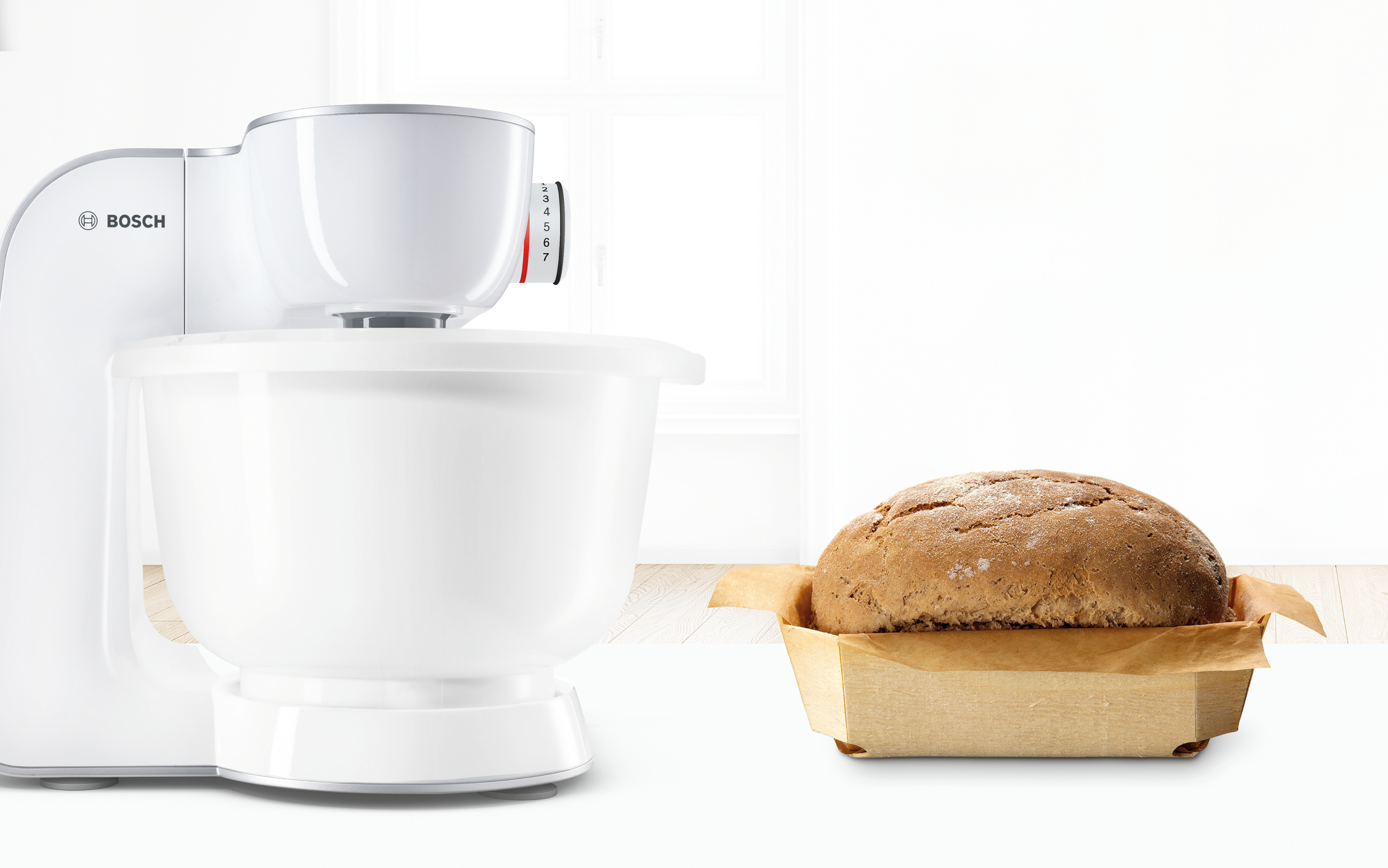 Ein weißer Küchenmixer und ein Brotlaib in einem Holzbehälter. Weiße und Holzfarben.