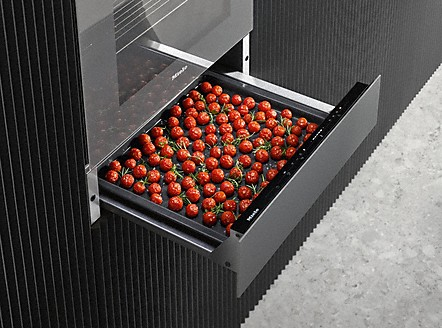 Ein Fach mit vielen roten Kirschtomaten auf einem schwarzen Blech.