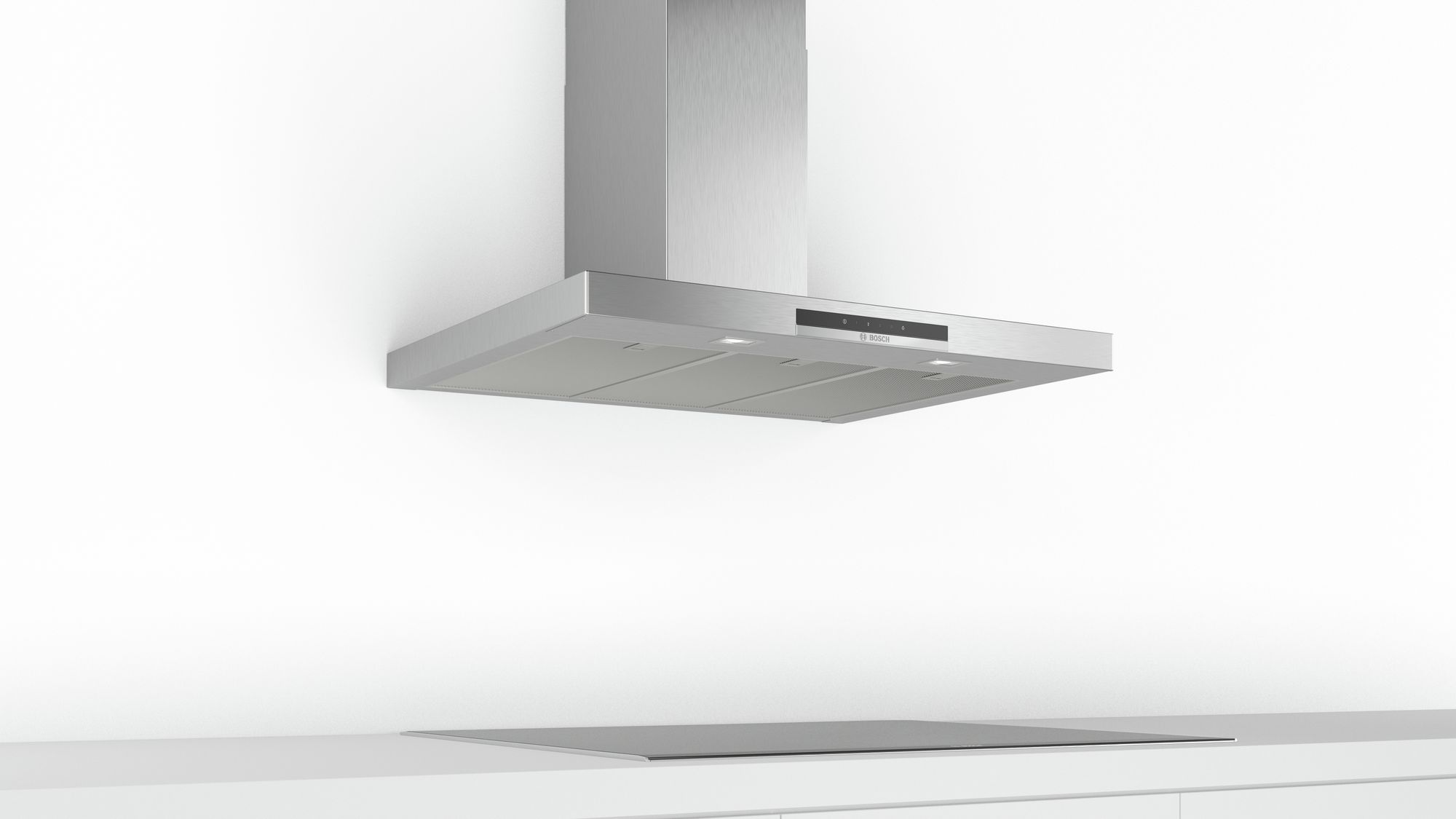 Une hotte de cuisine en acier inoxydable au-dessus d'une table de cuisson noire sur un mur blanc.