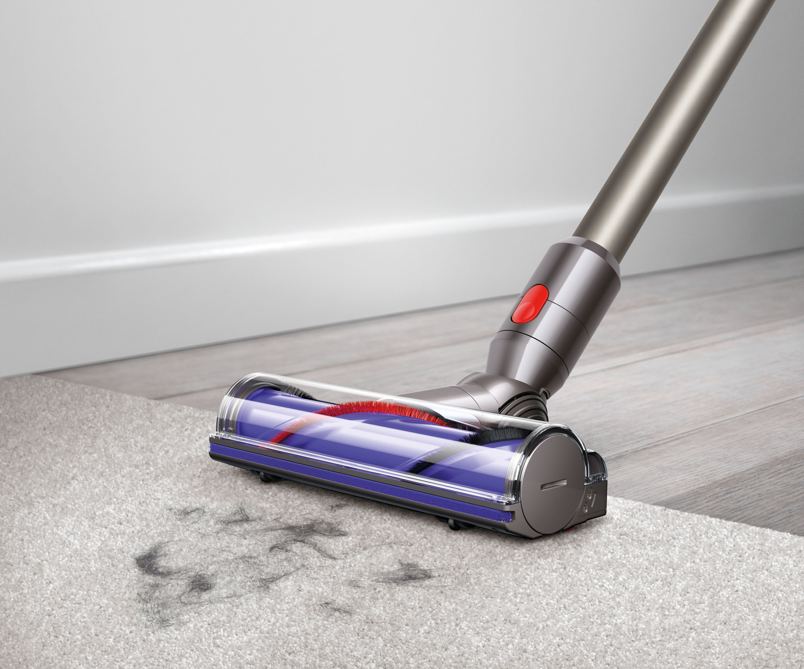 Dyson-Staubsauger reinigt einen Teppich. Der Kopf ist auf dem Teppich und nimmt Schmutz auf. Weiße Wand im Hintergrund.