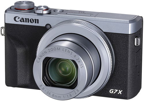 Ezüst és fekete Canon G7X kamera. Van rajta egy objektív és egy tárcsa a tetején.