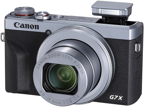 Ezüst és fekete Canon G7X kamera vakuval. Fehér háttér előtt.