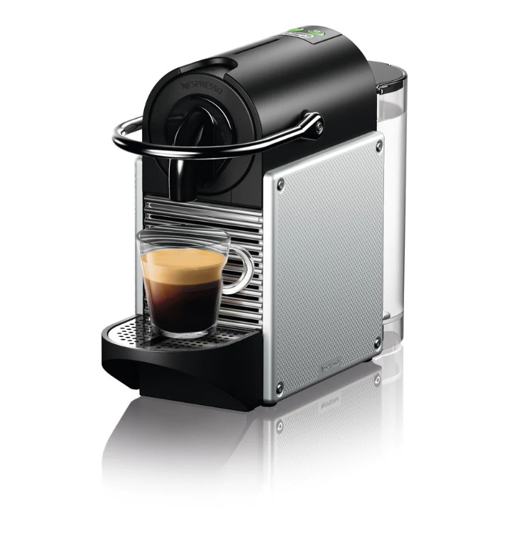 Schwarze und silberne Nespresso-Kaffeemaschine. Glas Kaffee vorne.
