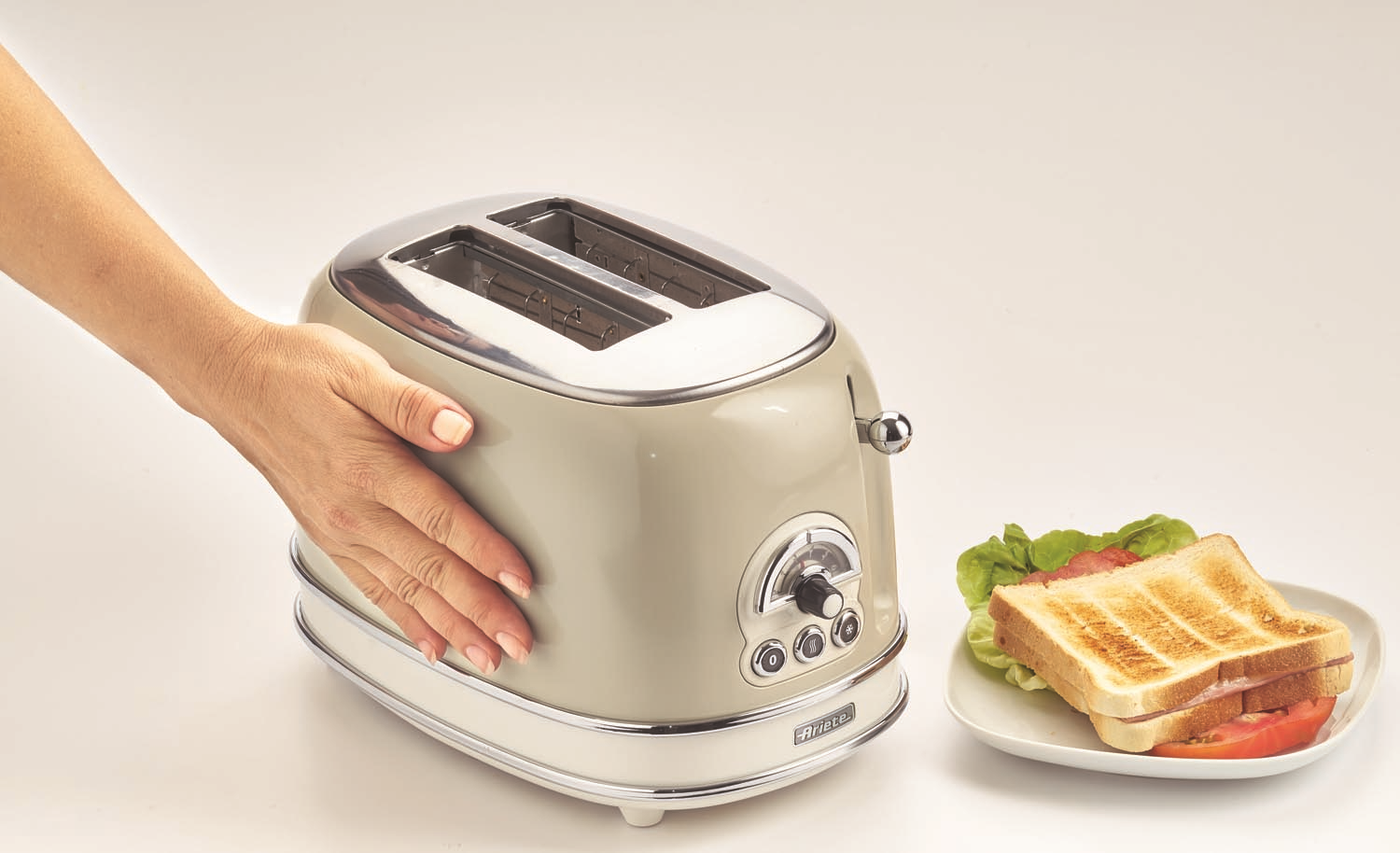 Toaster mit Hand daneben und Teller mit getoastetem Brot. Weißer Hintergrund.