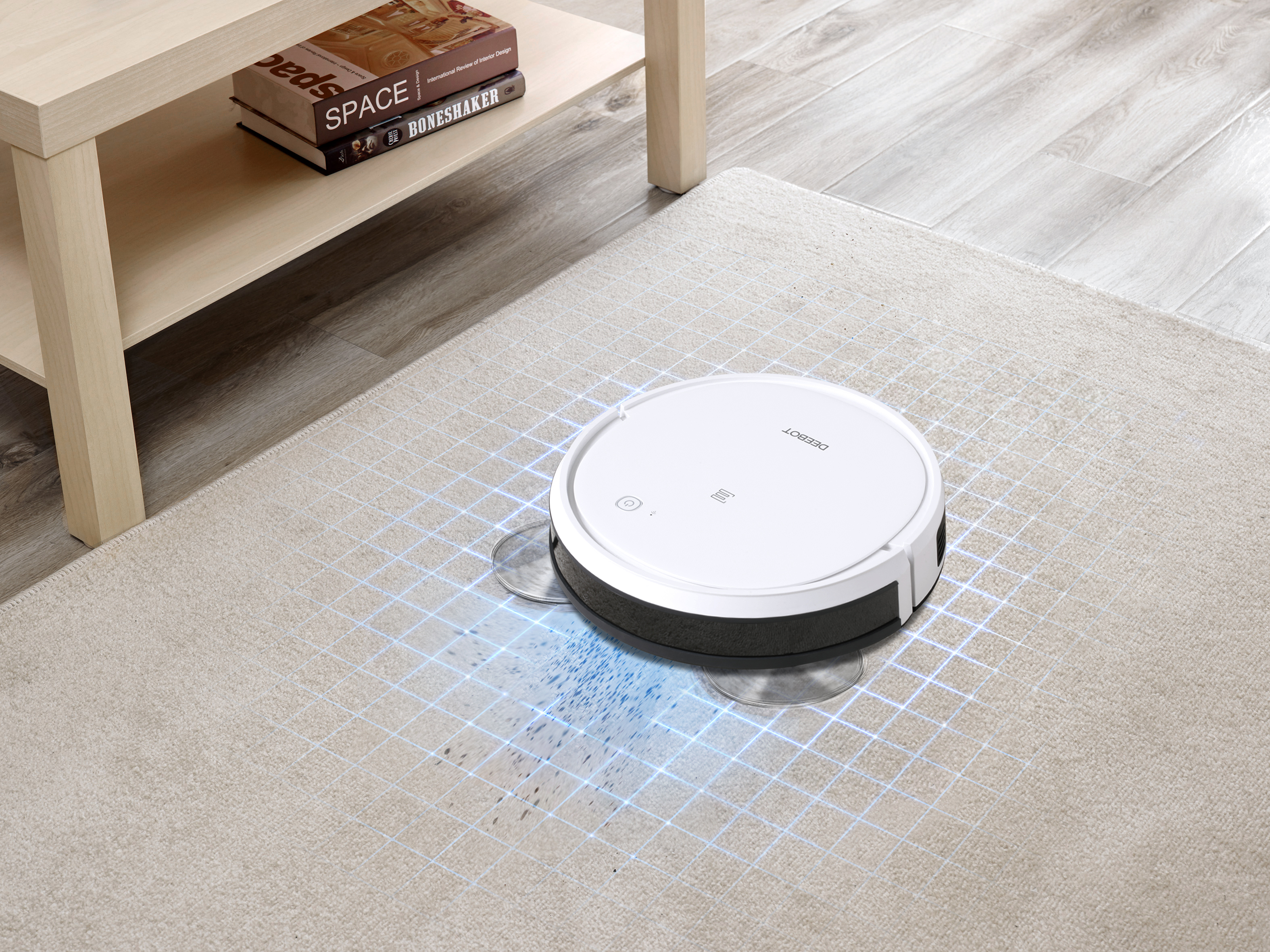 Roboter-Staubsauger auf einem Teppich, der putzt. Ein Tisch und Bücher sind im Hintergrund.