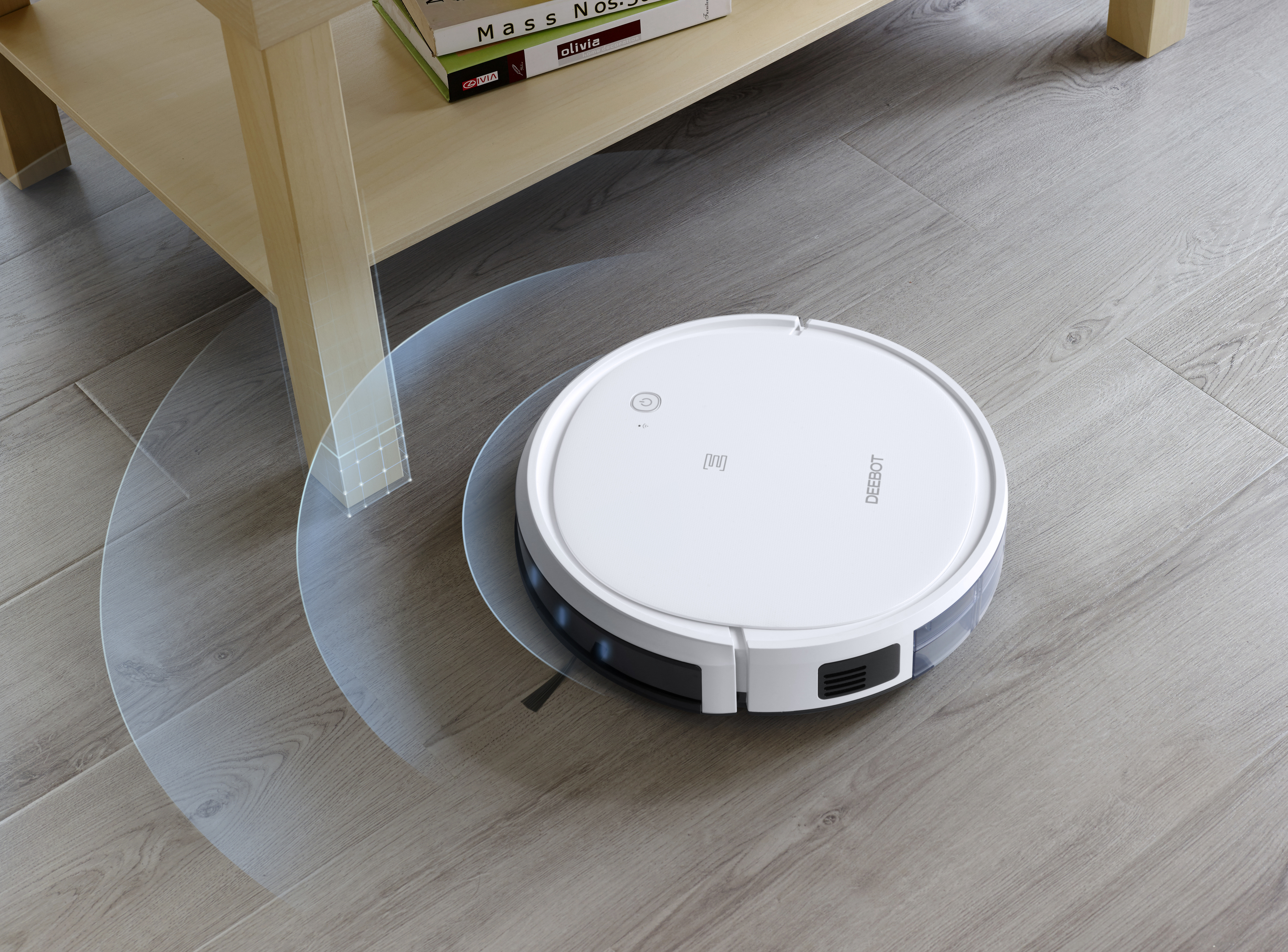 Roboter-Staubsauger beim Putzen, in der Nähe eines Tisches. Der Staubsauger ist weiß, auf Holzboden.