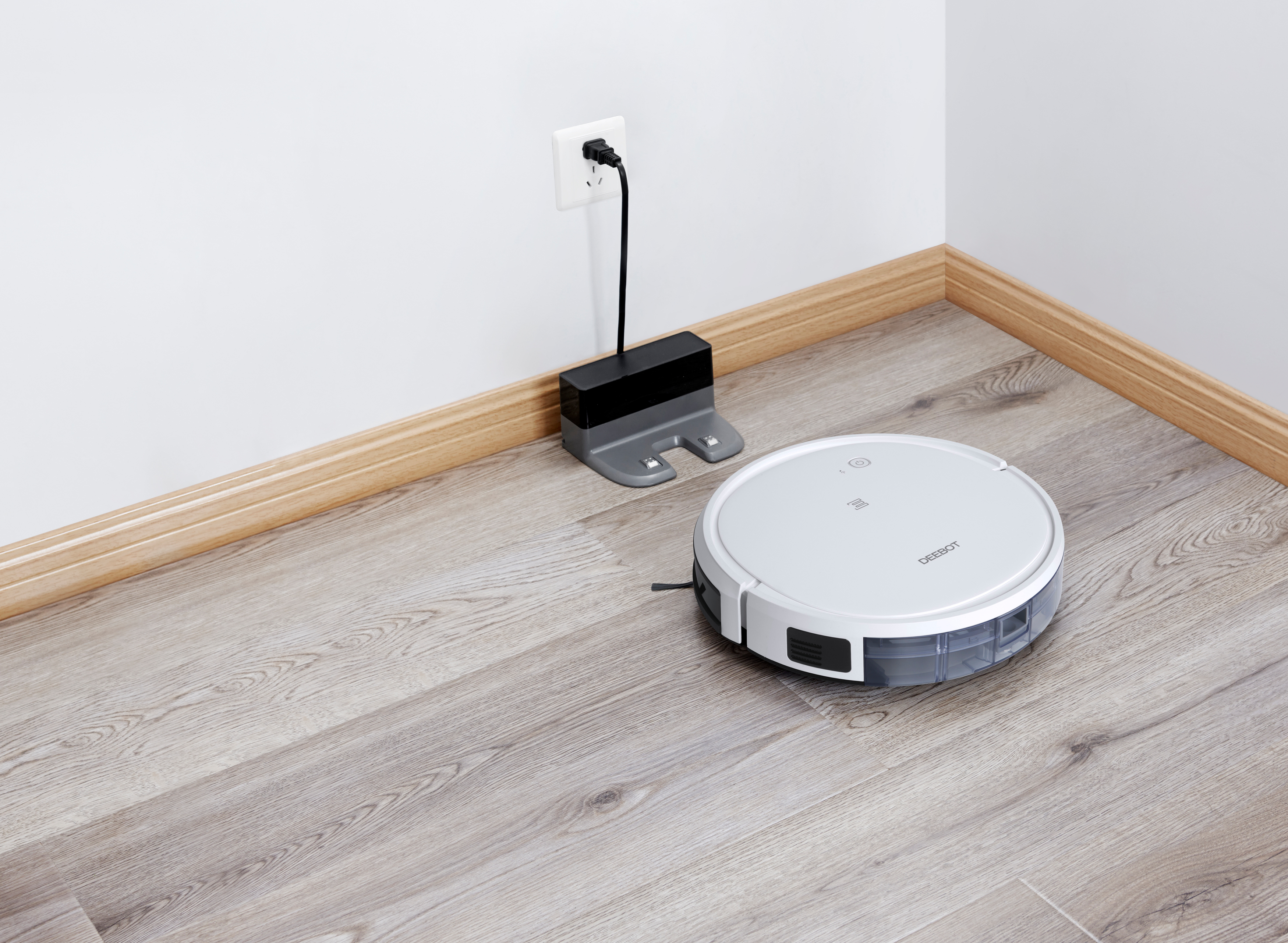 Ein weißer Roboter-Staubsauger neben seiner Ladestation. Die Ladestation ist eingesteckt.