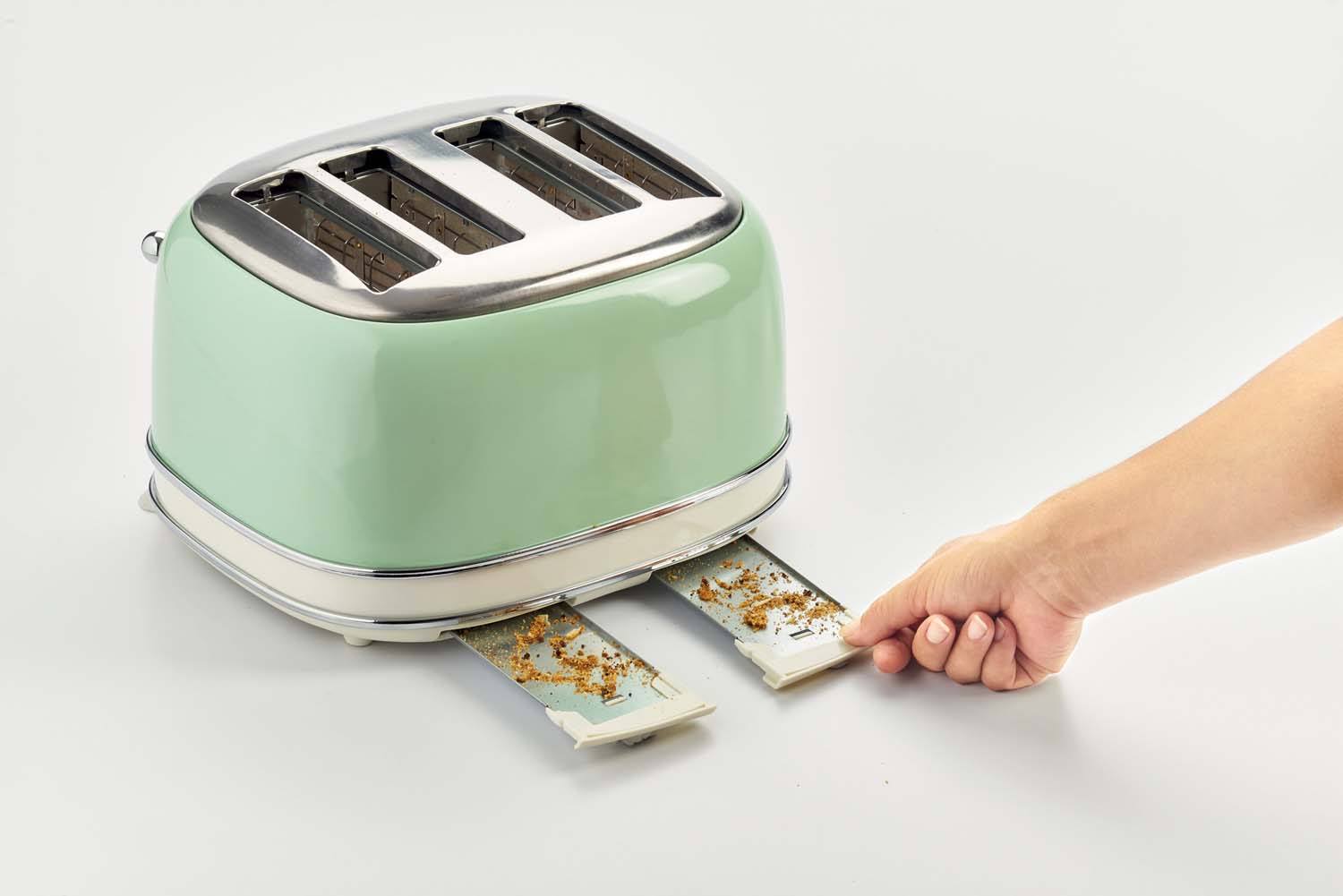 Grille-pain vert et argenté avec des miettes dans les plateaux, et une main.