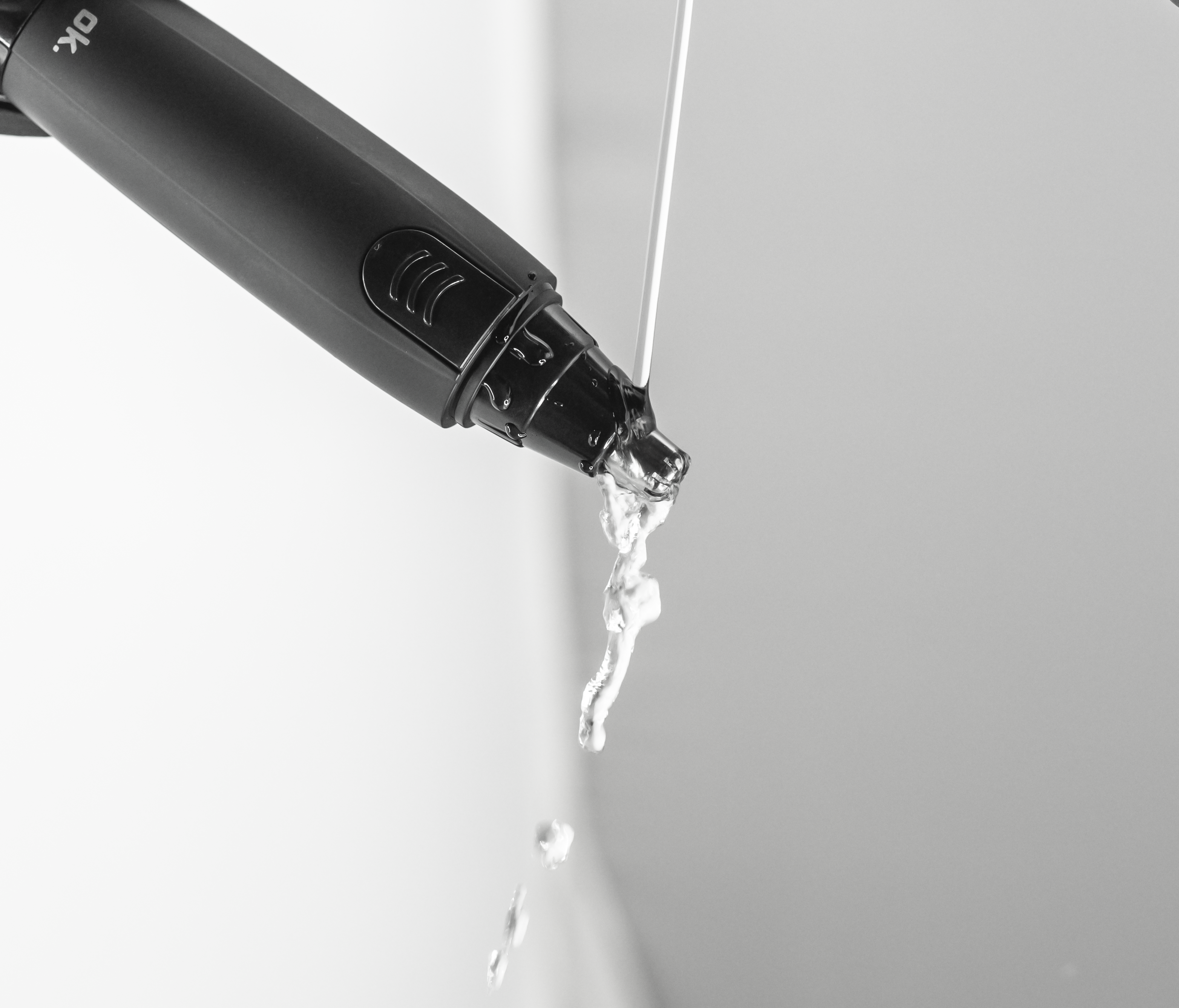 Ein grauer Haartrimmer mit weißer Flüssigkeit, die aus der Spitze tropft, vor hellem Hintergrund.