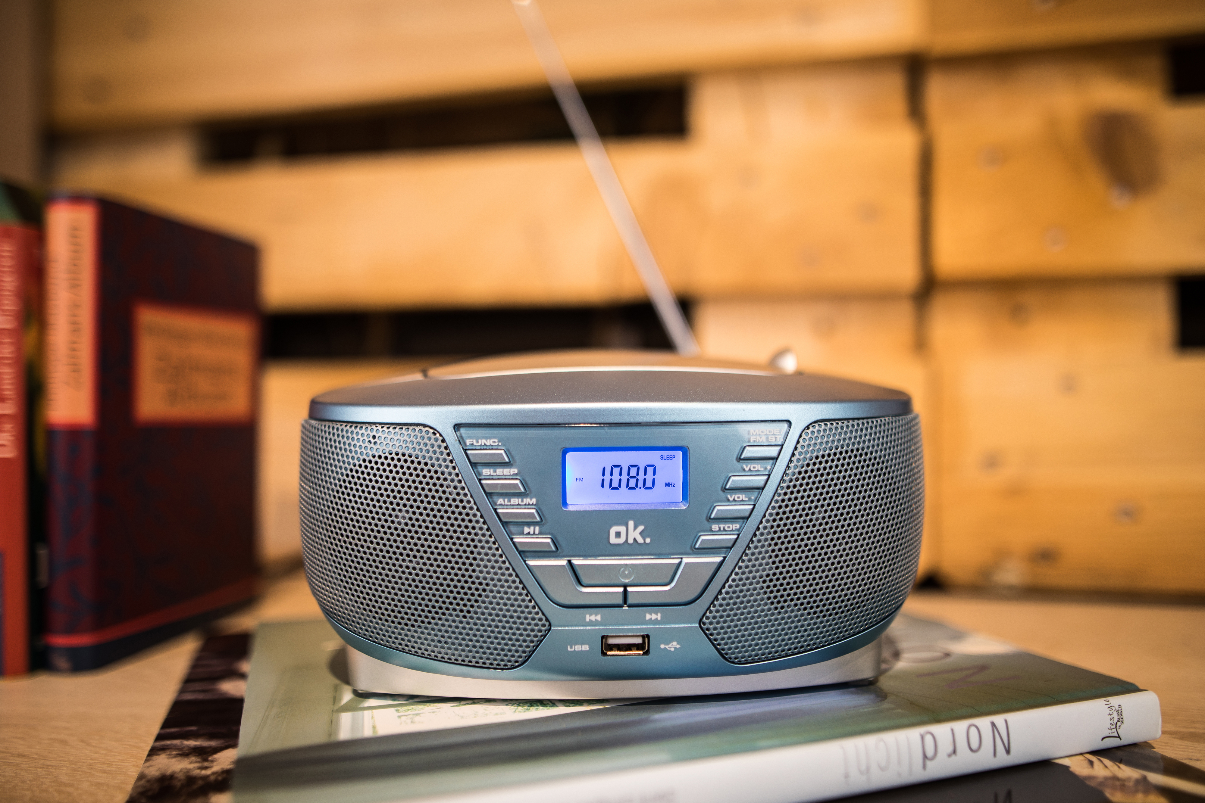 Ein kleines blaues Radio mit Digitalanzeige auf einem Buch, Holz-Hintergrund.