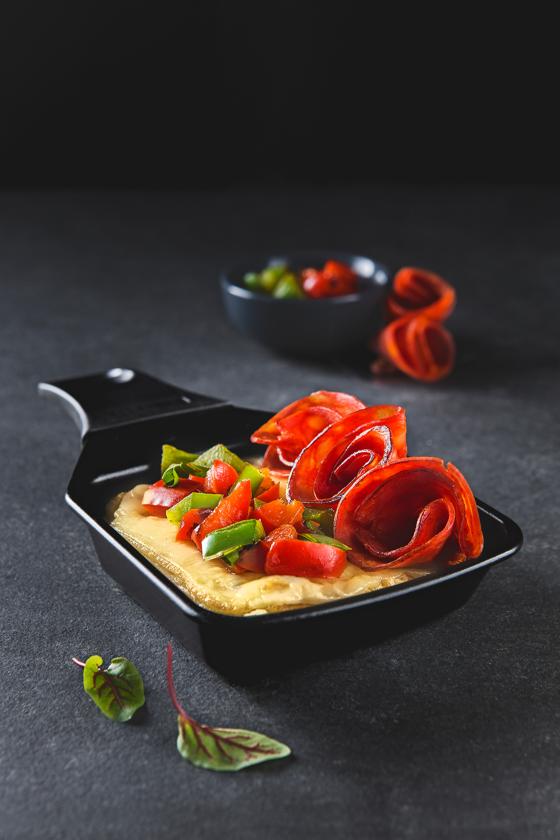 Ein Gericht mit roten Chorizo-Rosen, Gemüse und Sauce. Dunkler Hintergrund.