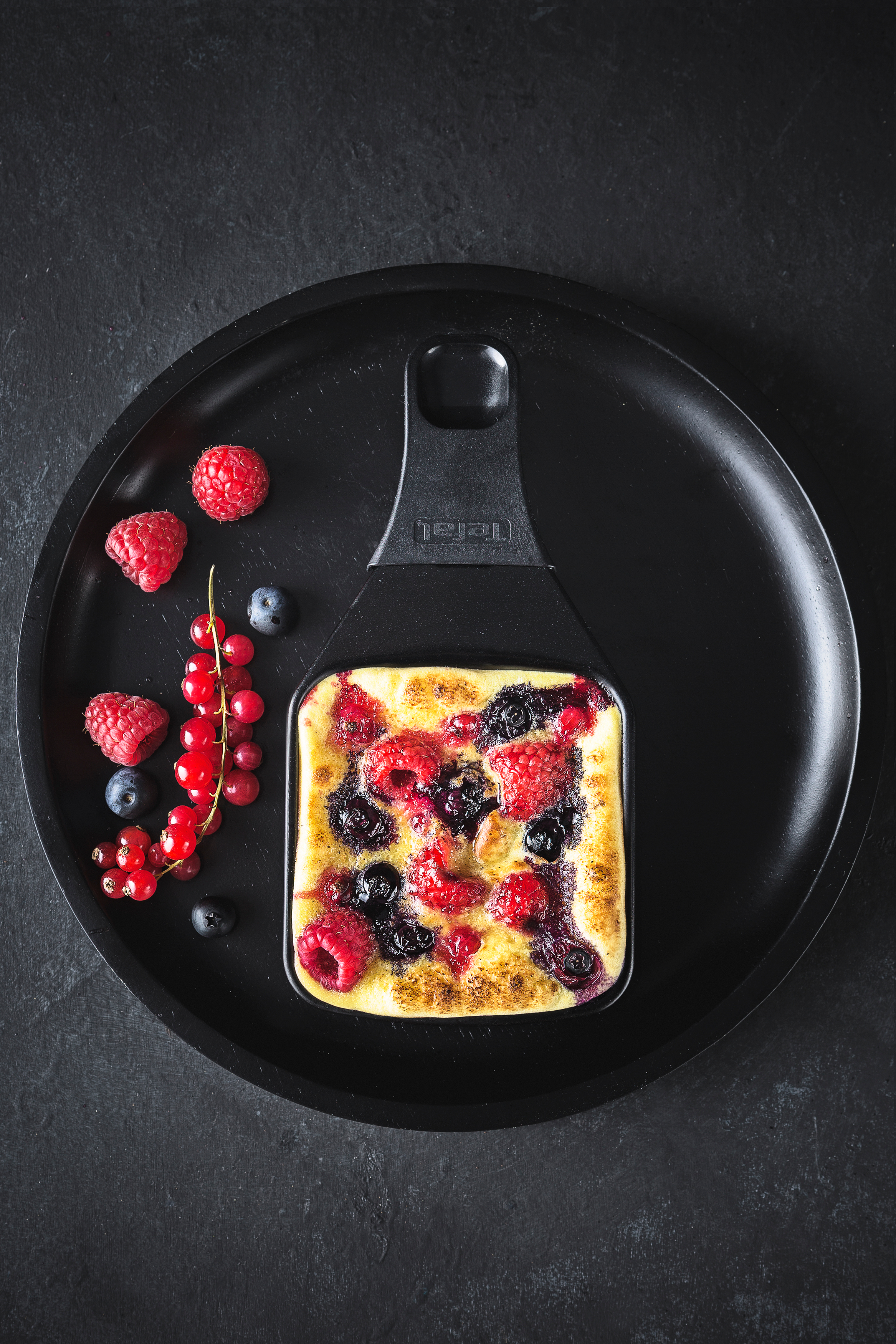 Gebackenes Fruchtdessert mit Himbeeren und Blaubeeren auf schwarzem Teller.