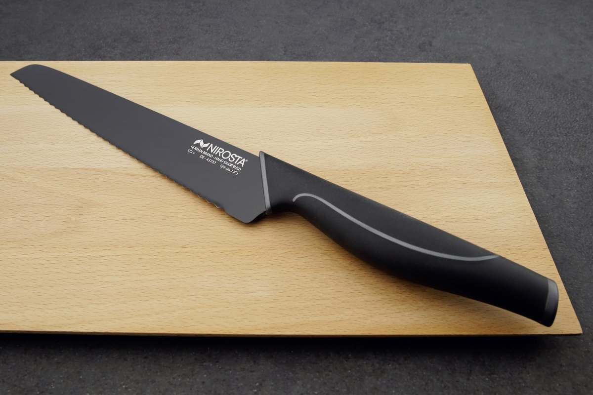 Schwarzes Messer mit gezahnter Klinge auf einem hellen Holzschneidebrett. Das Messer hat einen schwarzen Griff mit silbernem Detail.