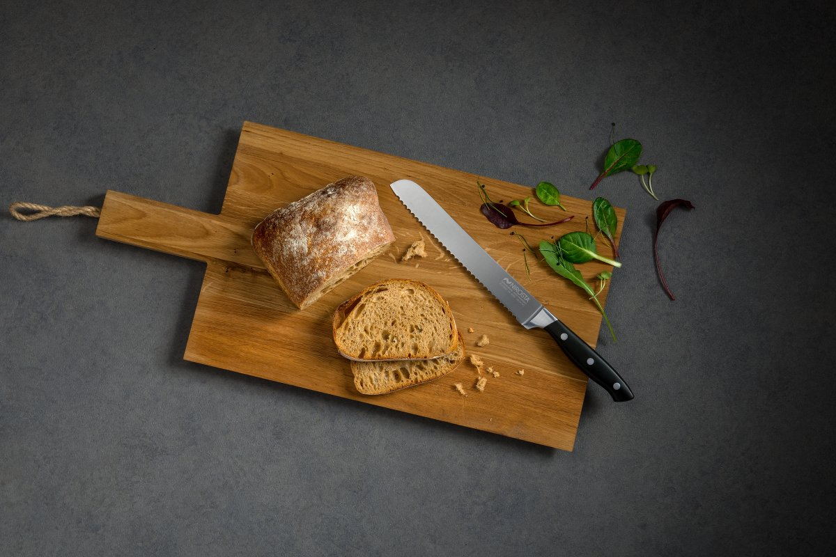 Holzschneidebrett mit Brotscheiben, einem Messer und Grünzeug auf grauer Oberfläche.