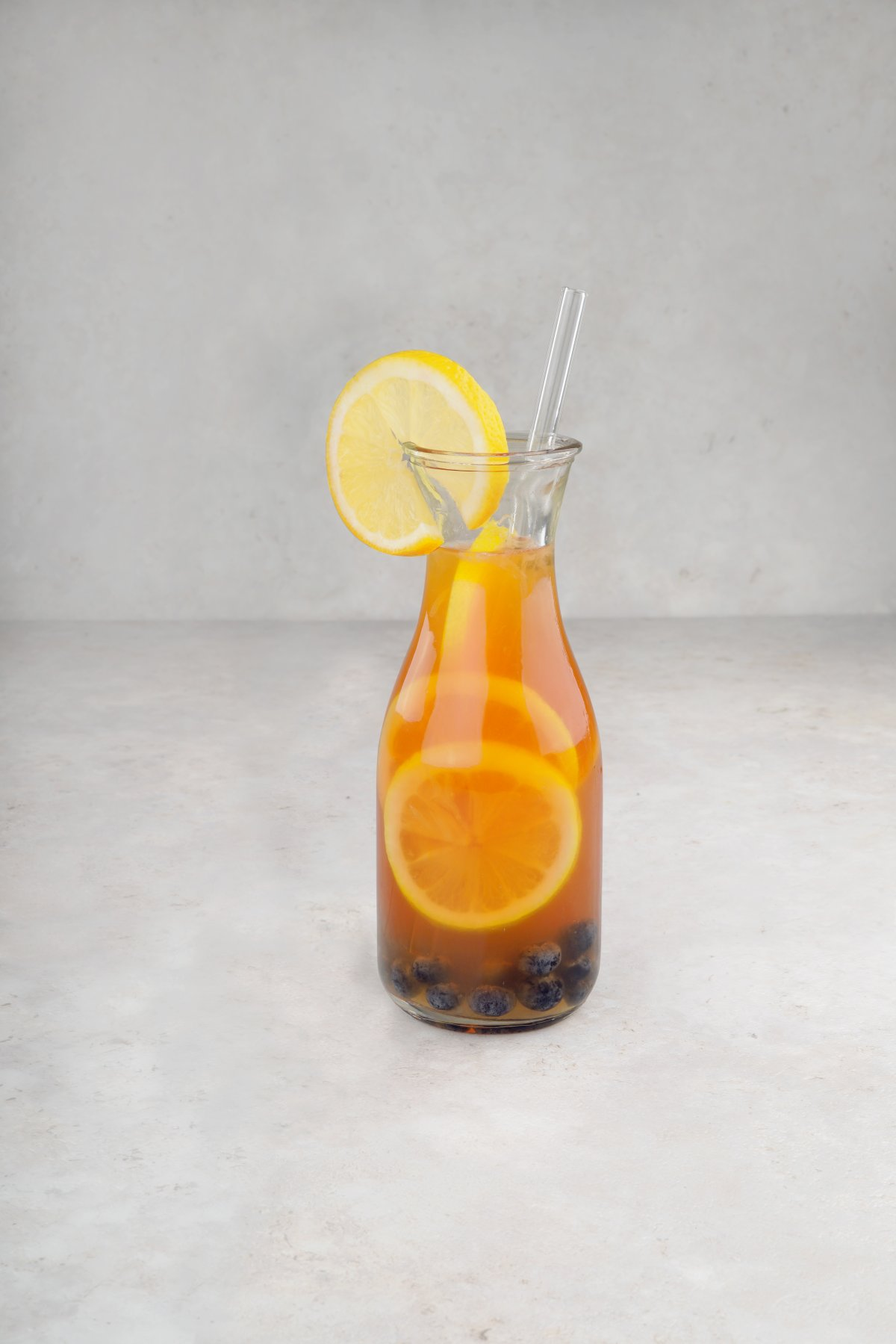 Eine Glasflasche mit einem orangenen Getränk, Zitronenscheiben, Blaubeeren und einem Strohhalm.
