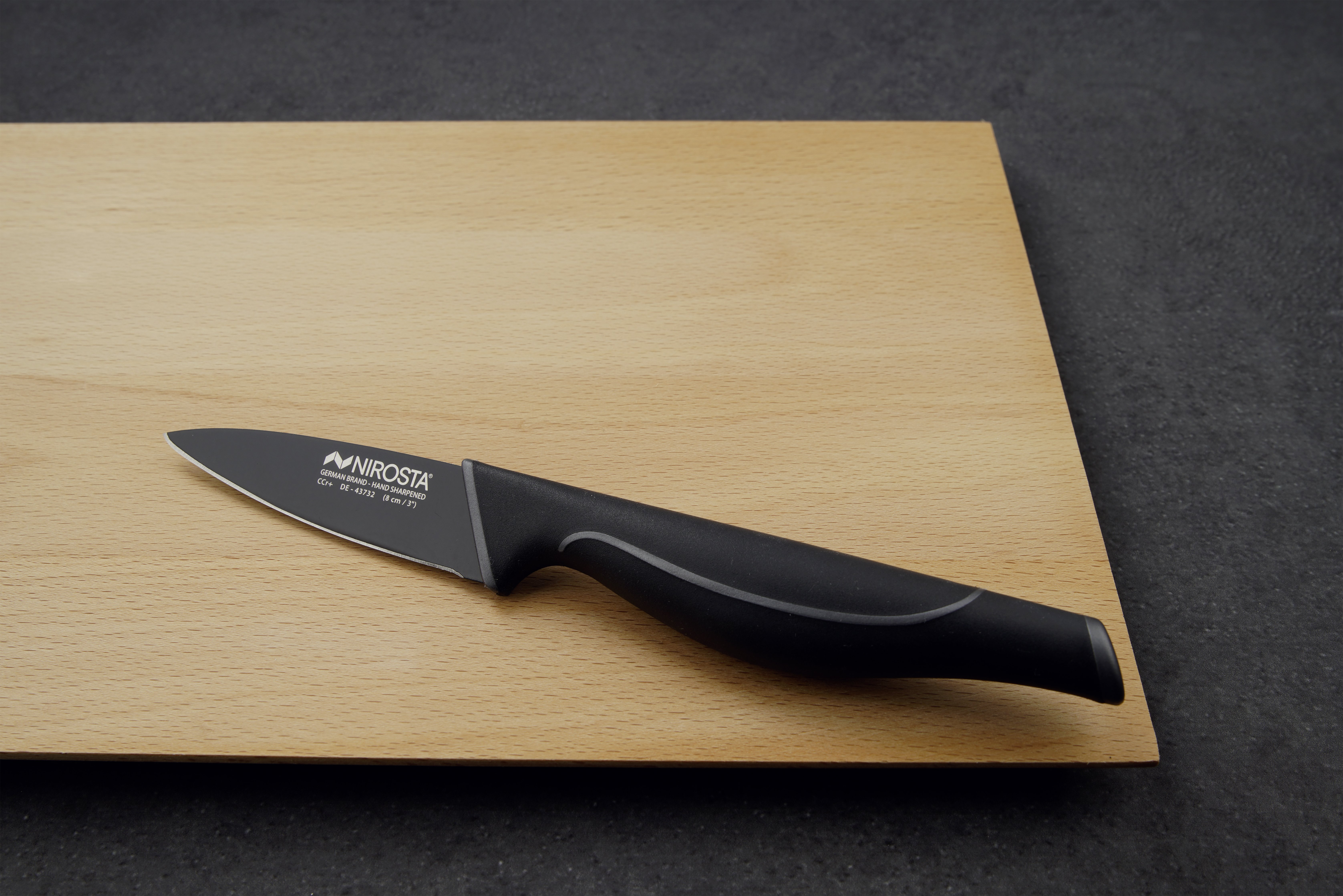 Ein schwarzes Messer auf einem hölzernen Schneidebrett. Der Hintergrund ist dunkelgrau.