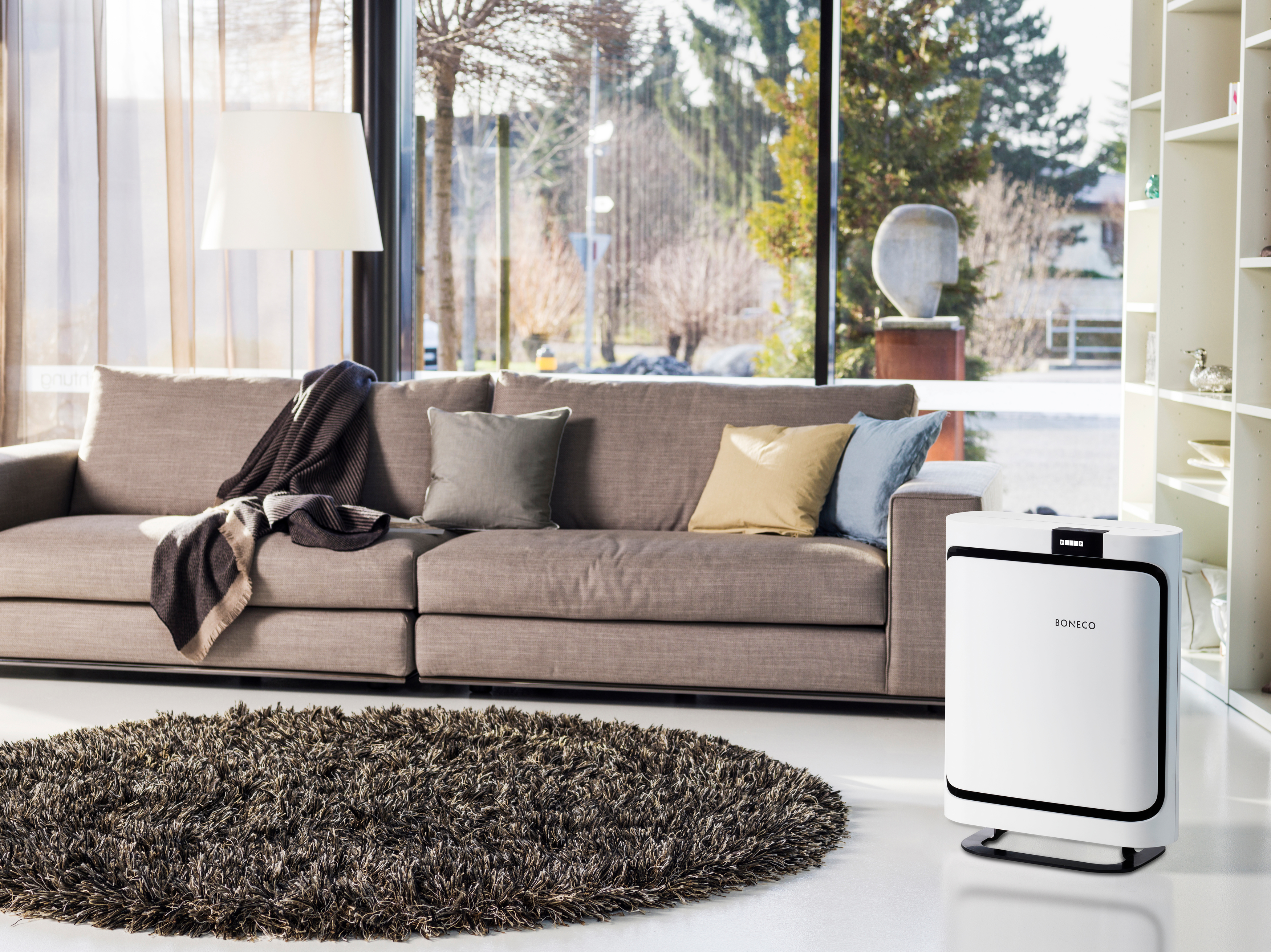 Wohnzimmer mit braunem Sofa, Teppich und Luftreiniger. Im Hintergrund ein großes Fenster.