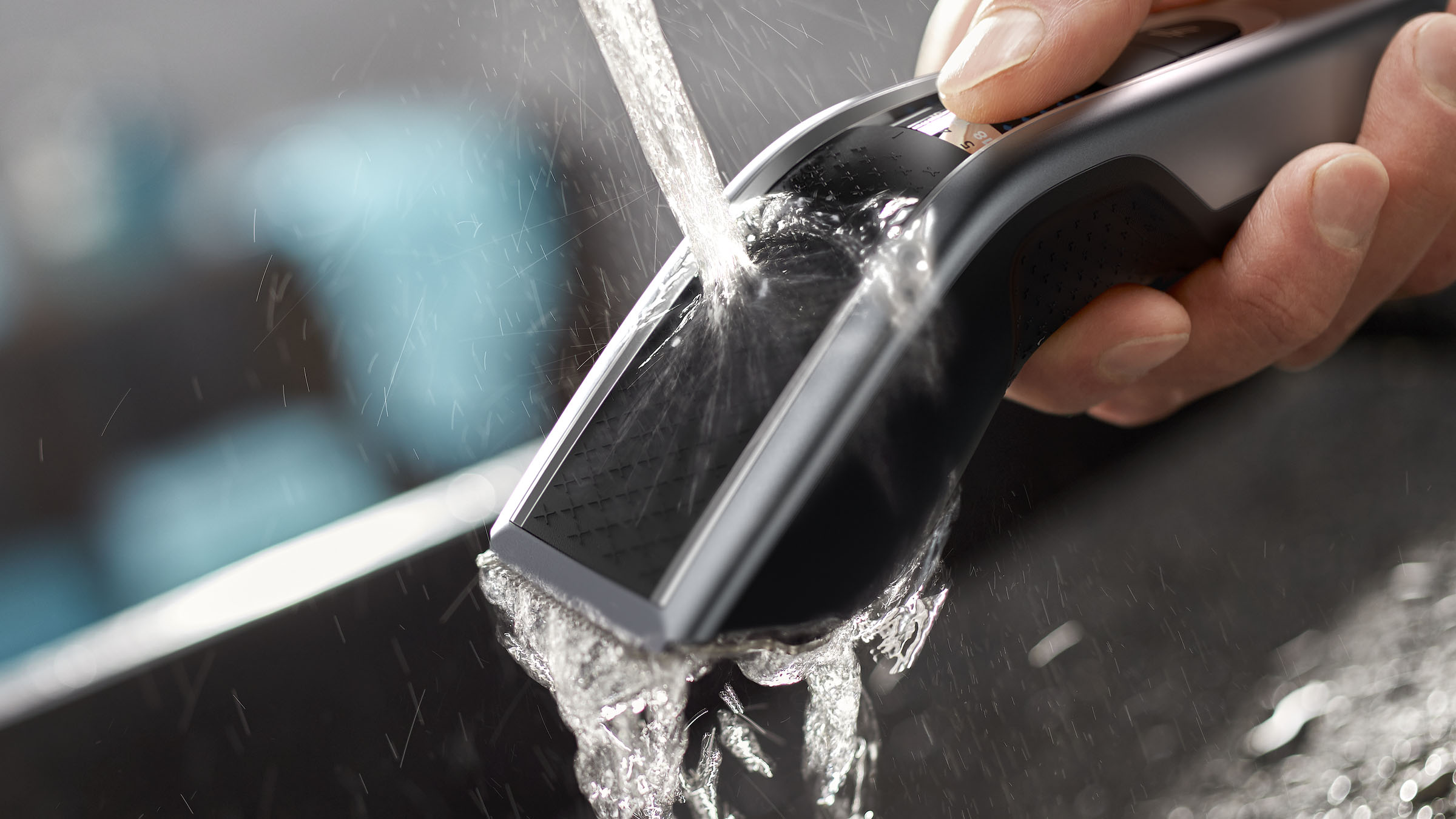 Nahaufnahme eines schwarzen Haarschneiders, der mit Wasser gespült wird. Die Klingen stehen im Fokus.