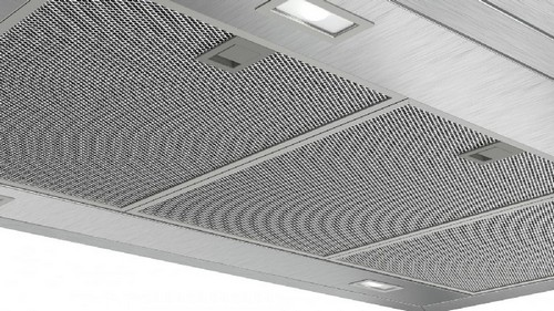 Una campana extractora de acero inoxidable con filtro de malla y luces empotradas se ve desde abajo.