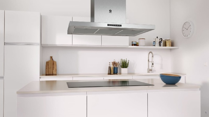 Cocina blanca moderna con campana extractora plateada y reloj.