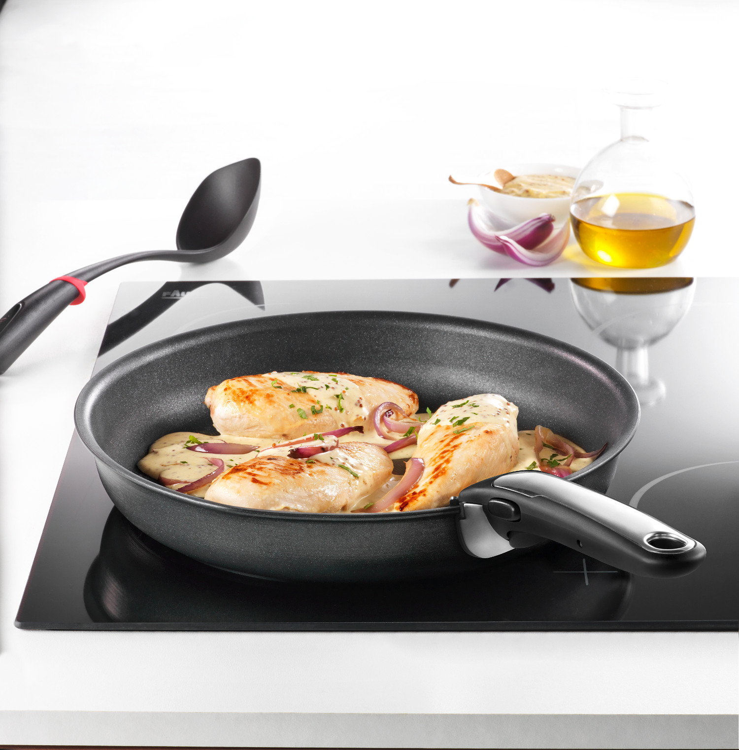 Poitrines de poulet avec sauce et oignons cuisant dans une poêle sur une cuisinière noire. Une cuillère, de l'huile et des condiments sont visibles.