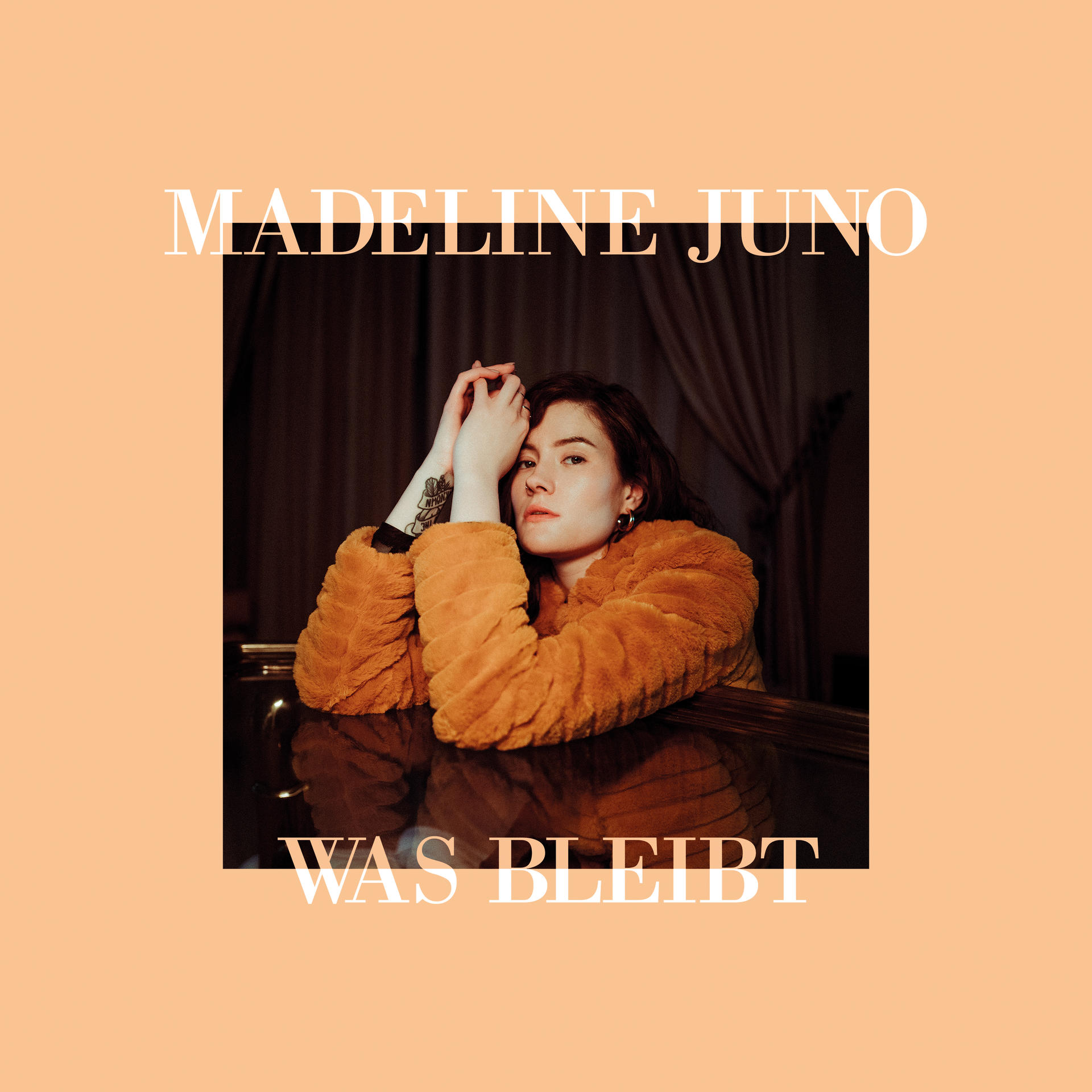 Albumcover mit Frau in orangefarbenem Pelzmantel. Text: 'MADELINE JUNO WAS BLEIBT'. Pfirsichfarbener Hintergrund.