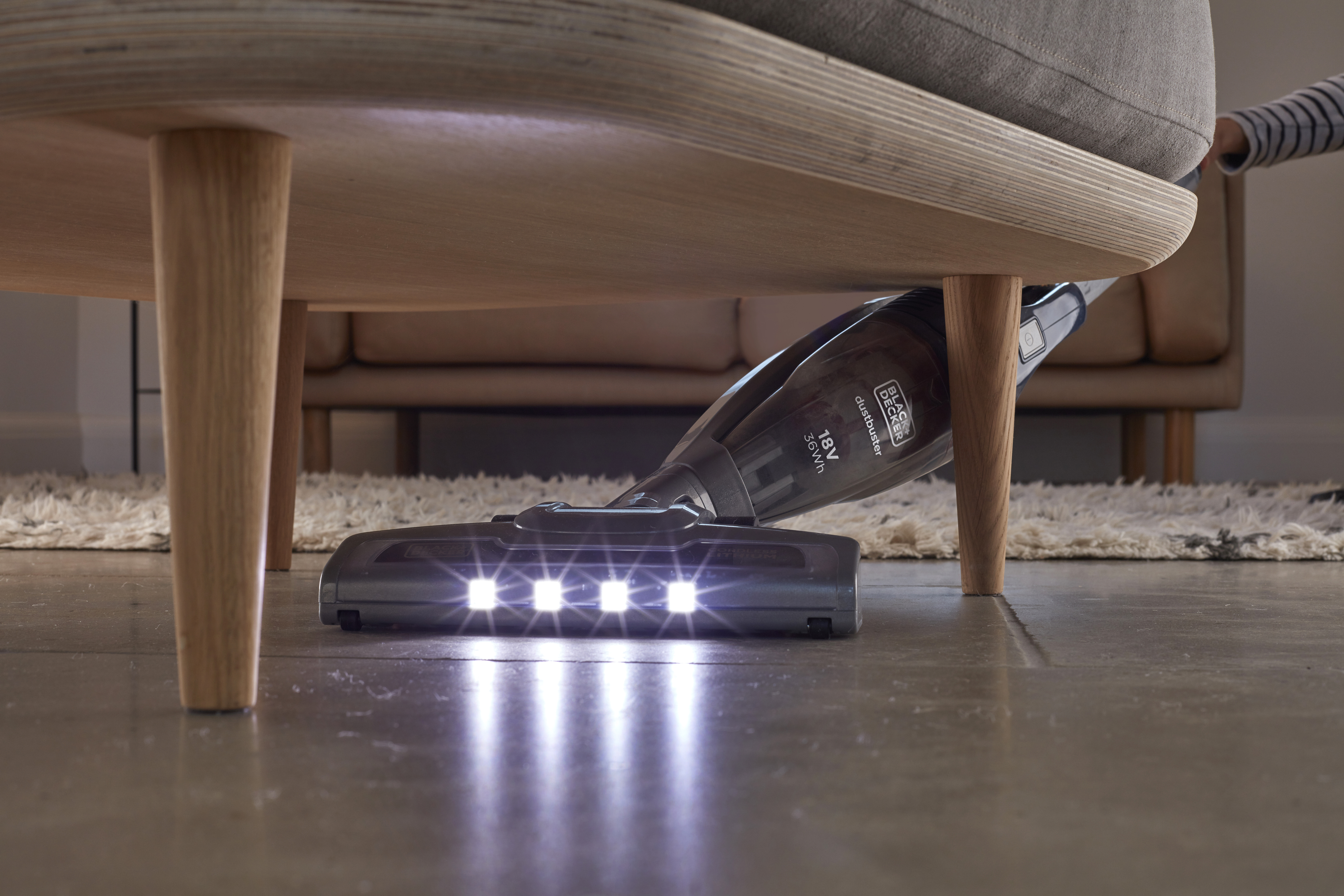 Staubsauger unter einem Sofa. Der Staubsauger hat Lichter.