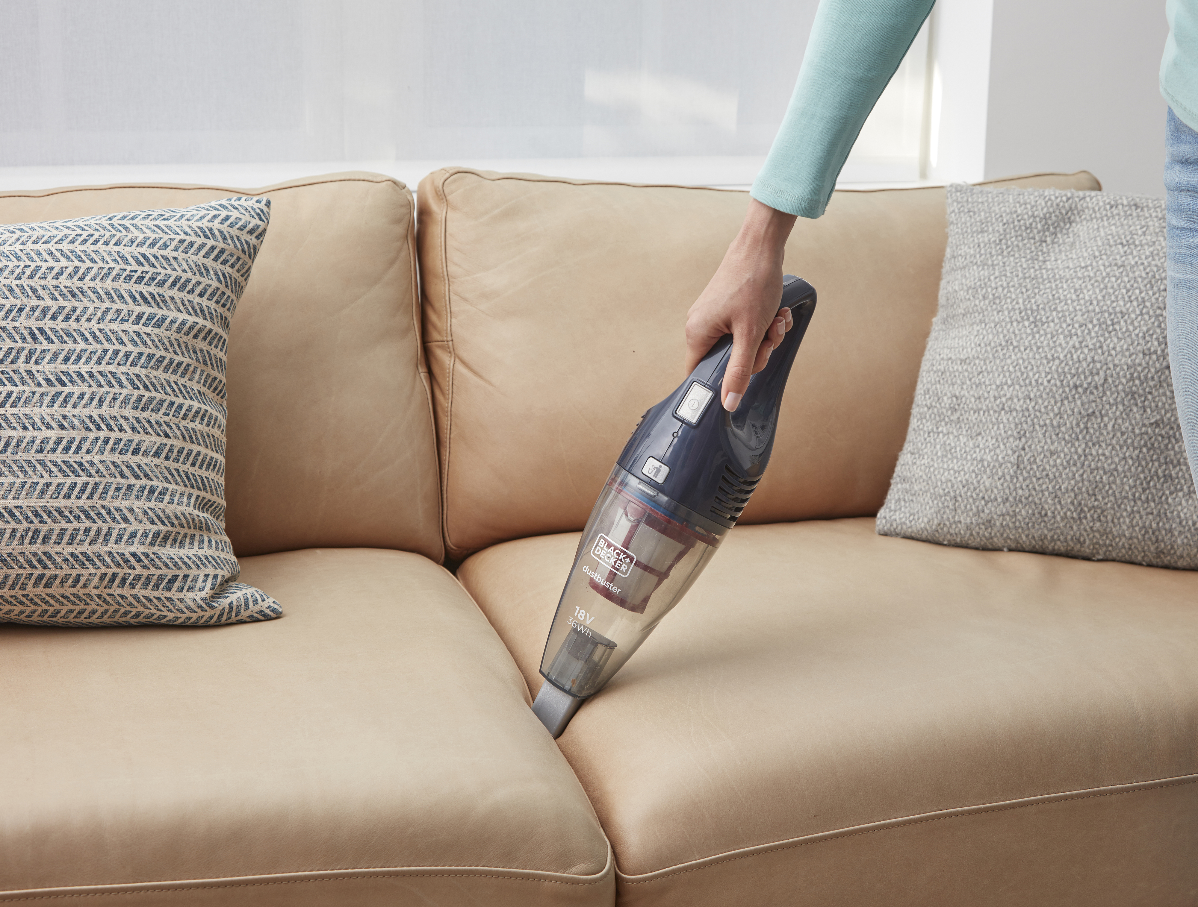 Ein Handstaubsauger reinigt die Naht einer Ledercouch. Der Staubsauger ist dunkelblau.
