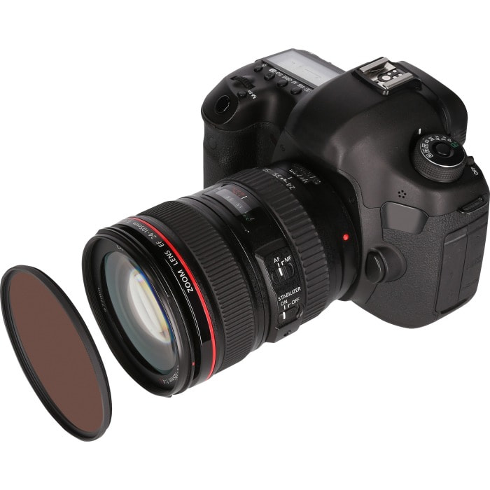 Een zwarte DSLR-camera met een grote lens bevestigd. Een bruin filter ligt naast de lens. Witte achtergrond.