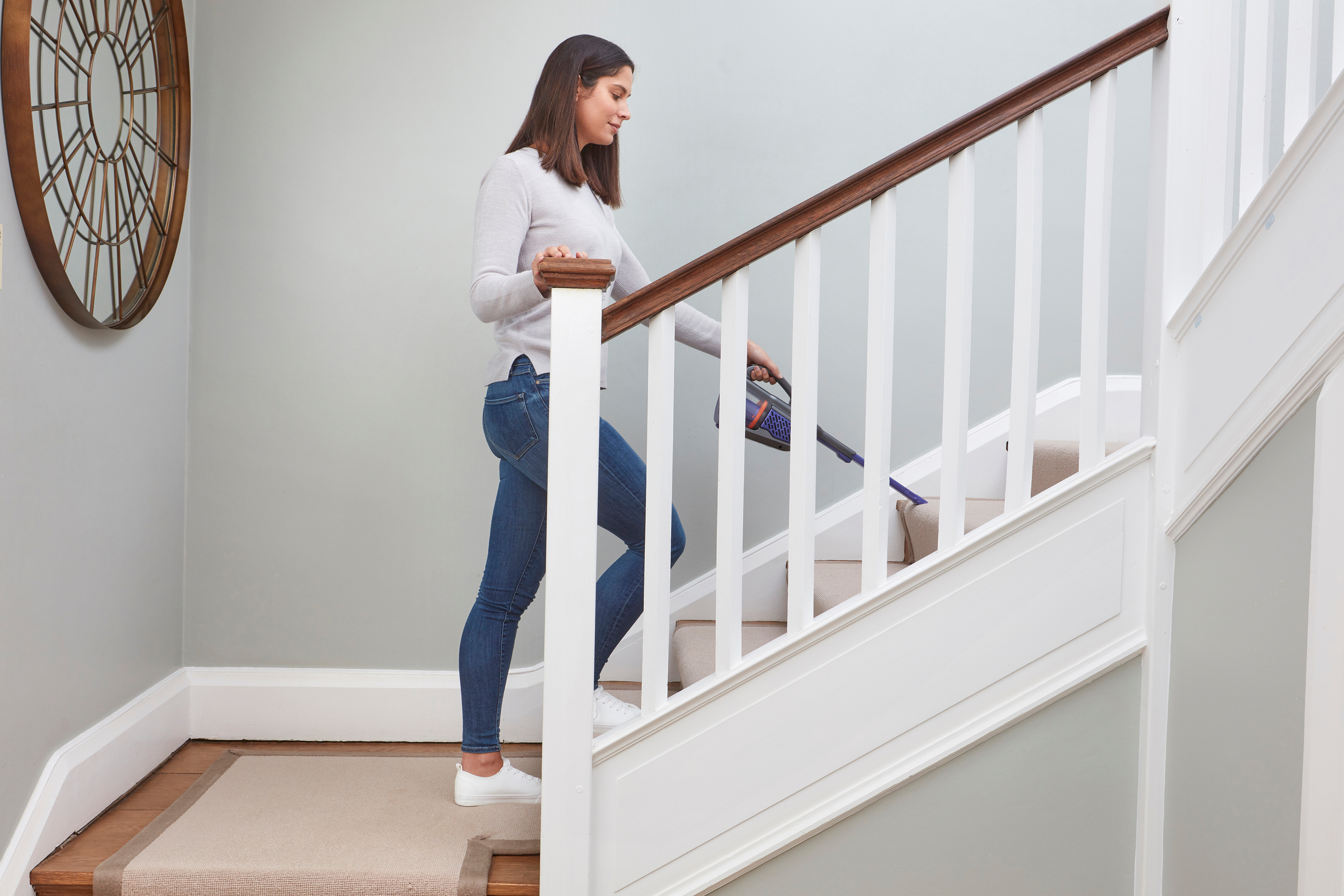 Frau, die Treppen saugt. Weißes Geländer und beiger Teppich. Hellgraue Wände.